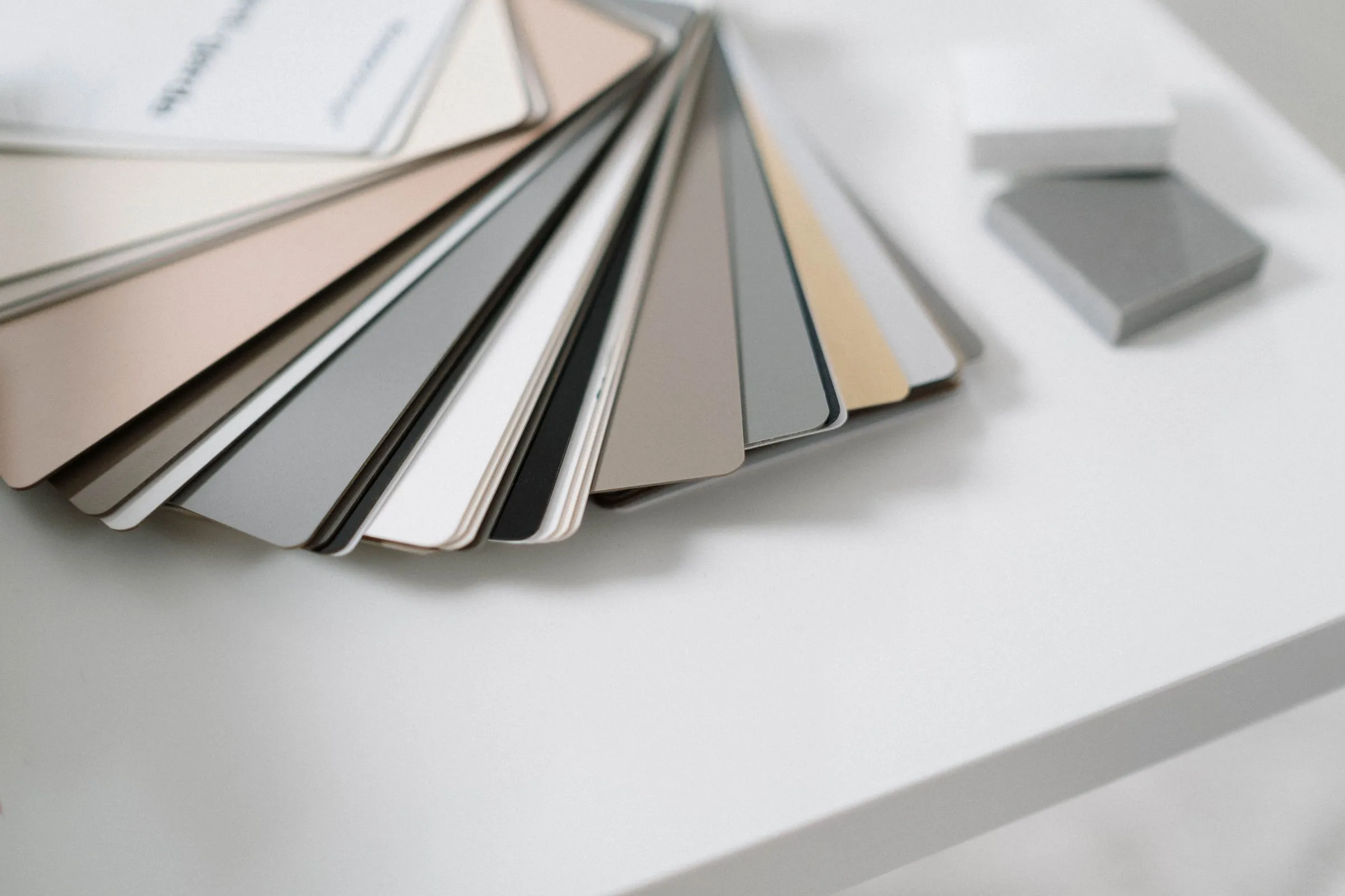 Fan of neutral colour and material sample cards in beige, grey and white on a white table.