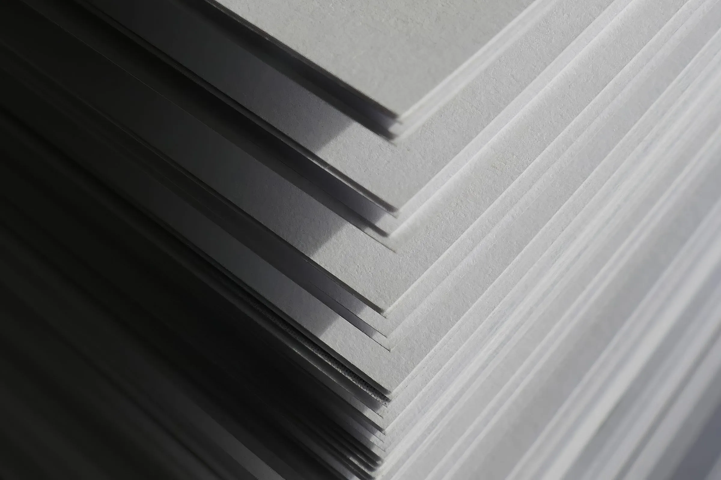 Close-up of a stack of white paper sheets fanned in steps, fading from dark to light grey.