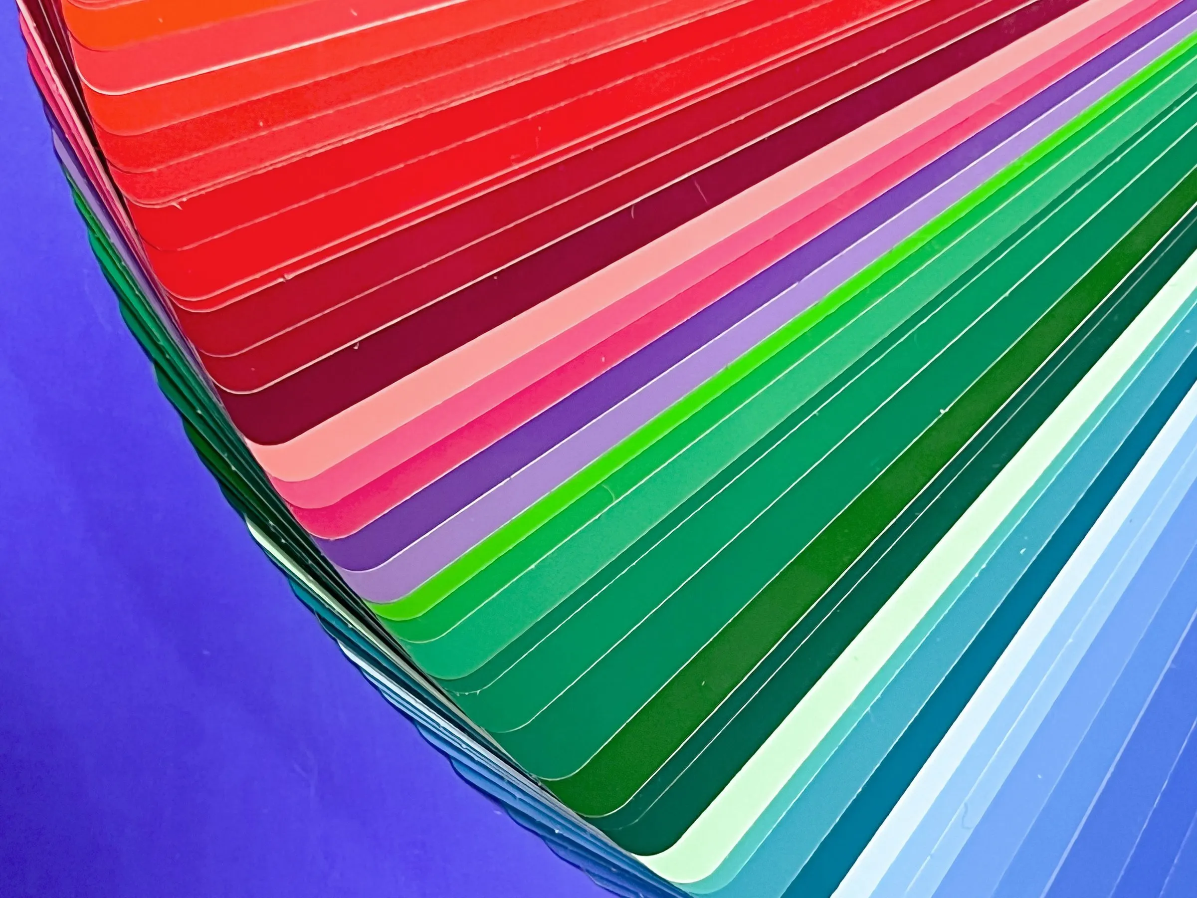 A fan of paint color swatch cards in reds, pinks, greens and blues spread over a violet background.