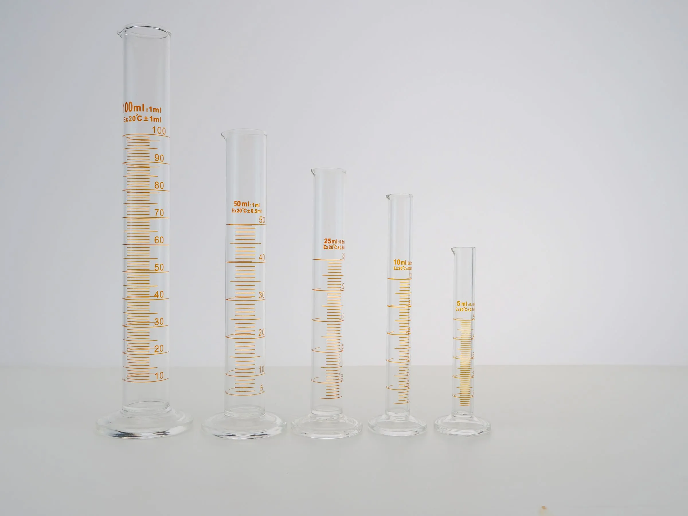 Row of glass graduated cylinders arranged from tallest to shortest on white.