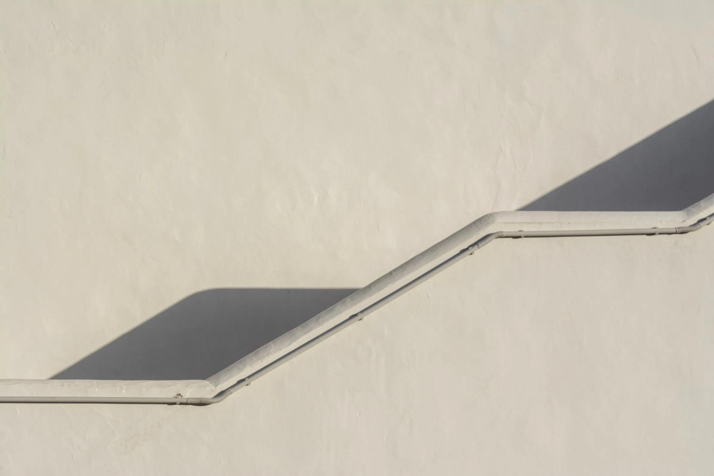 White handrail climbing a cream wall in steps, casting a dark shadow.