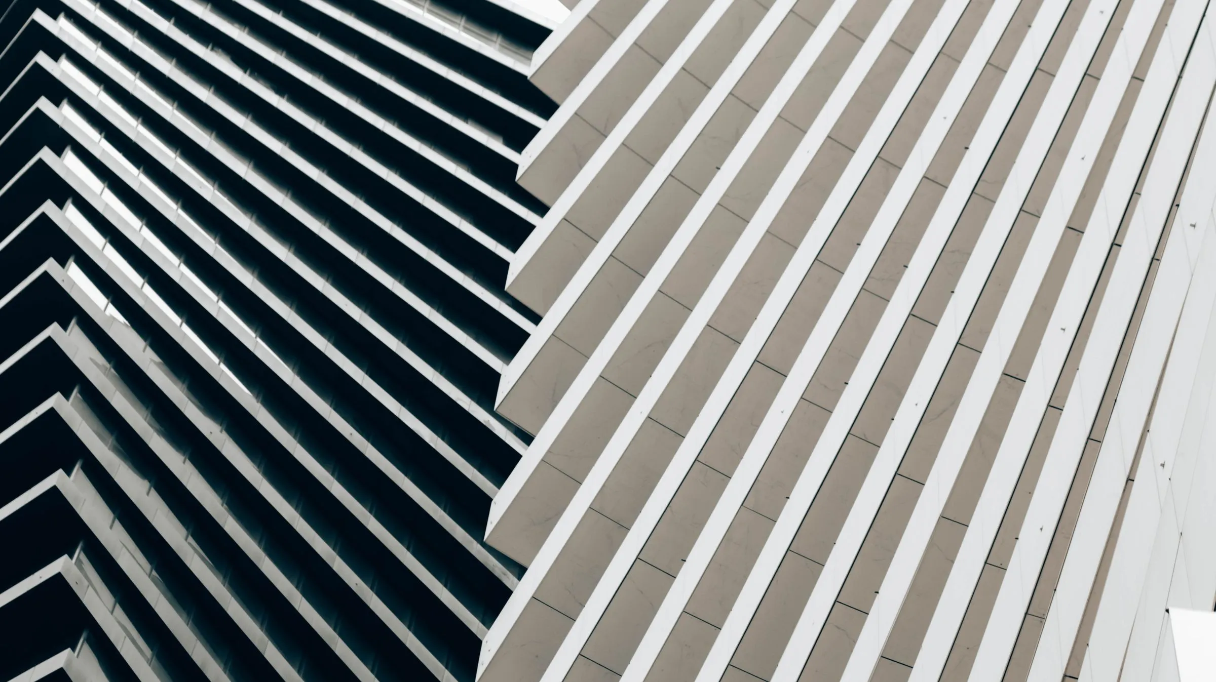 Two building facades of repeating horizontal fins, one dark and one pale, meeting diagonally.