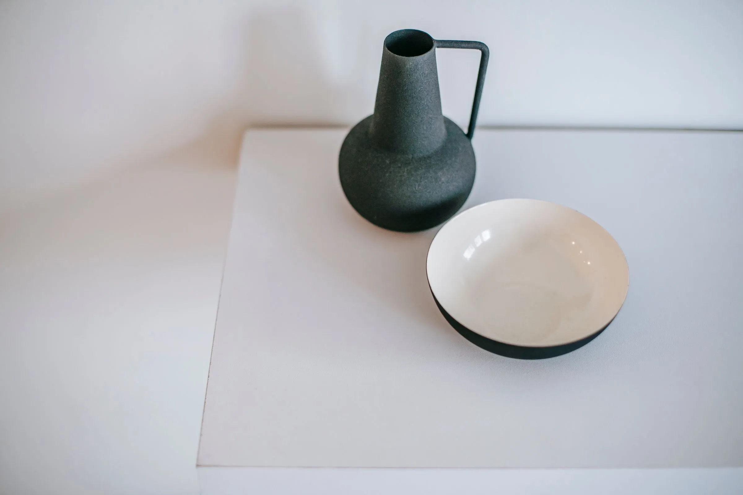 Dark green ceramic jug and a black-and-white bowl on a white surface.