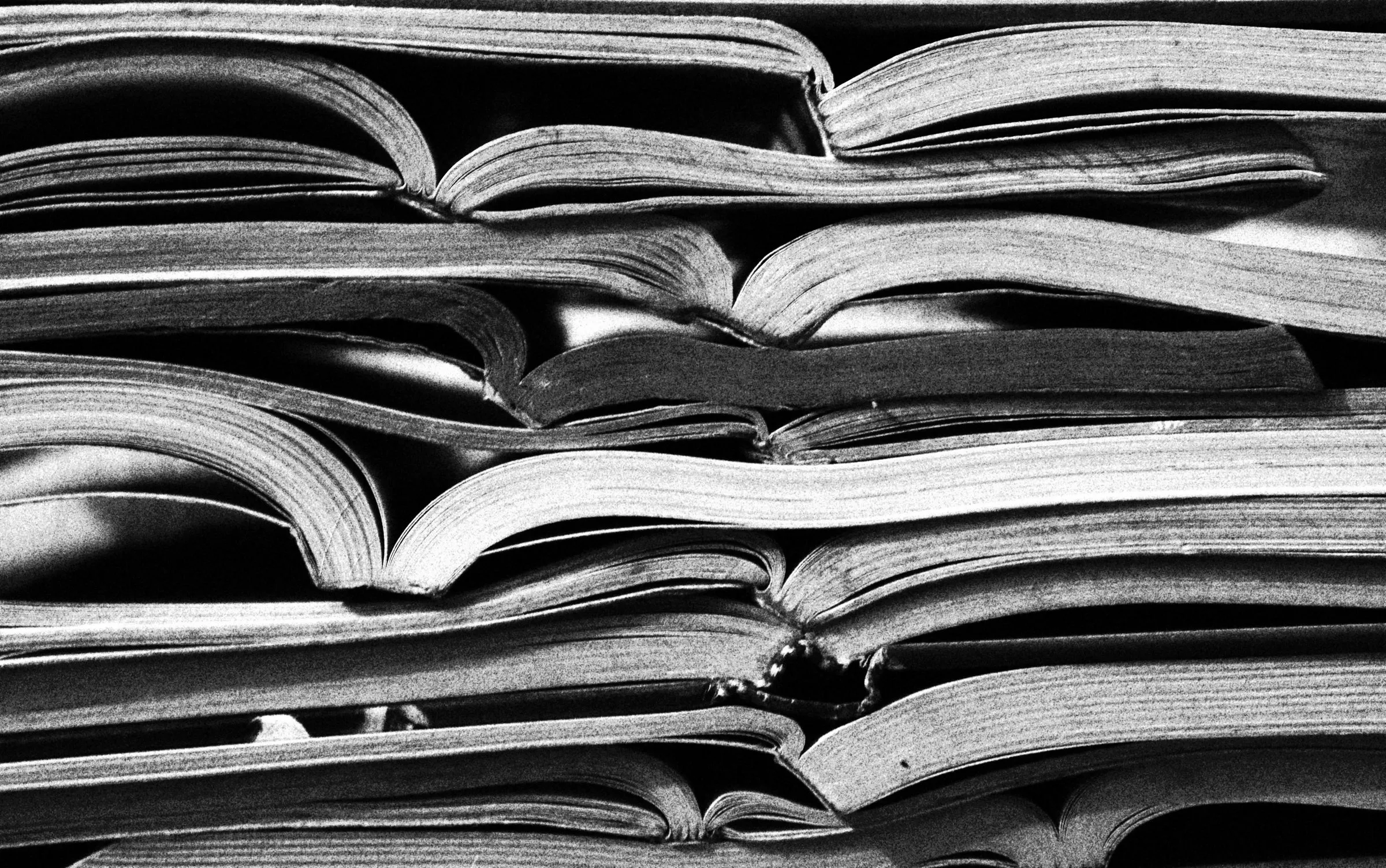 Black-and-white close-up of many open magazines stacked on top of each other.