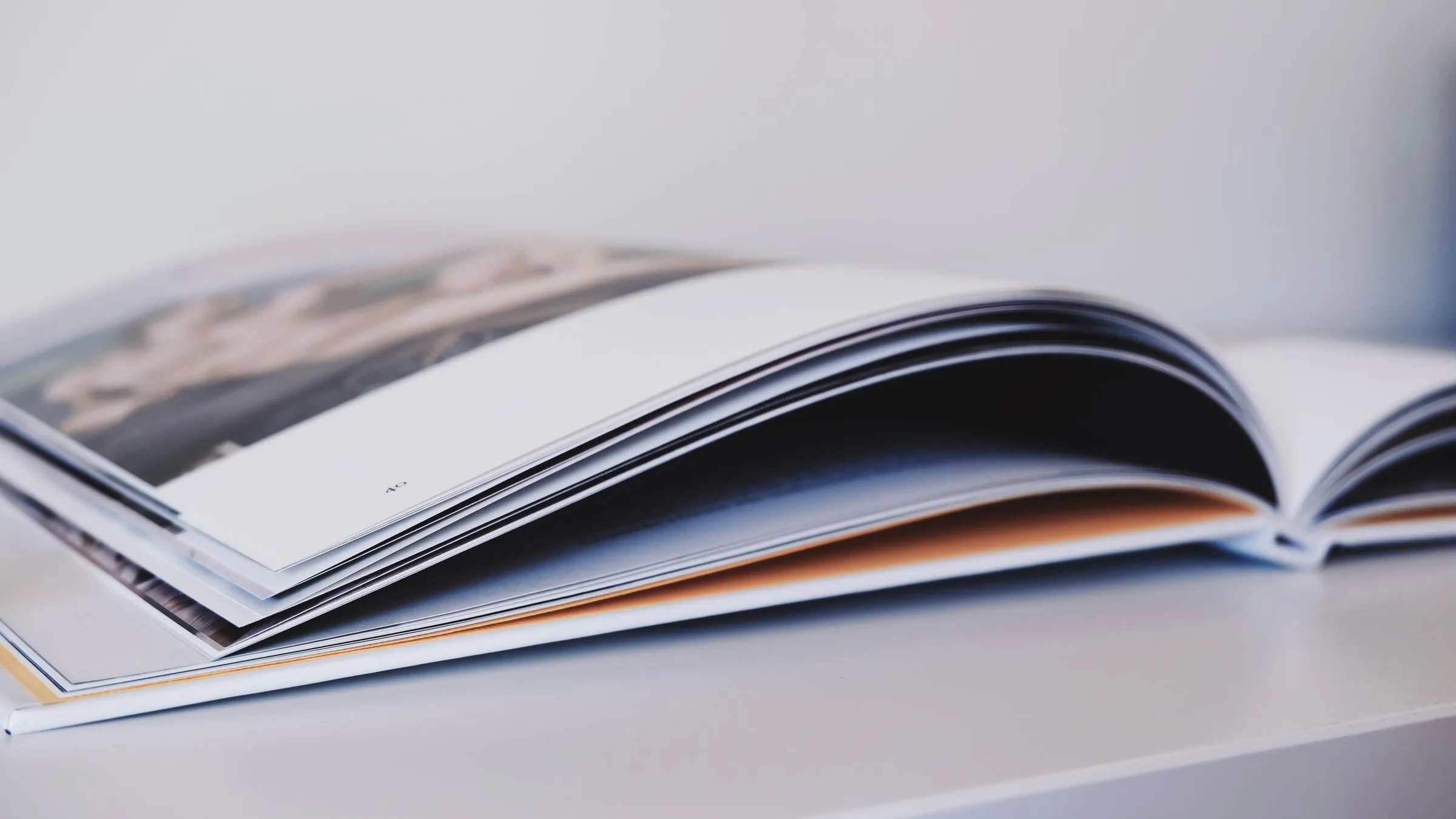 Thick printed book open on a white shelf, pages fanned.