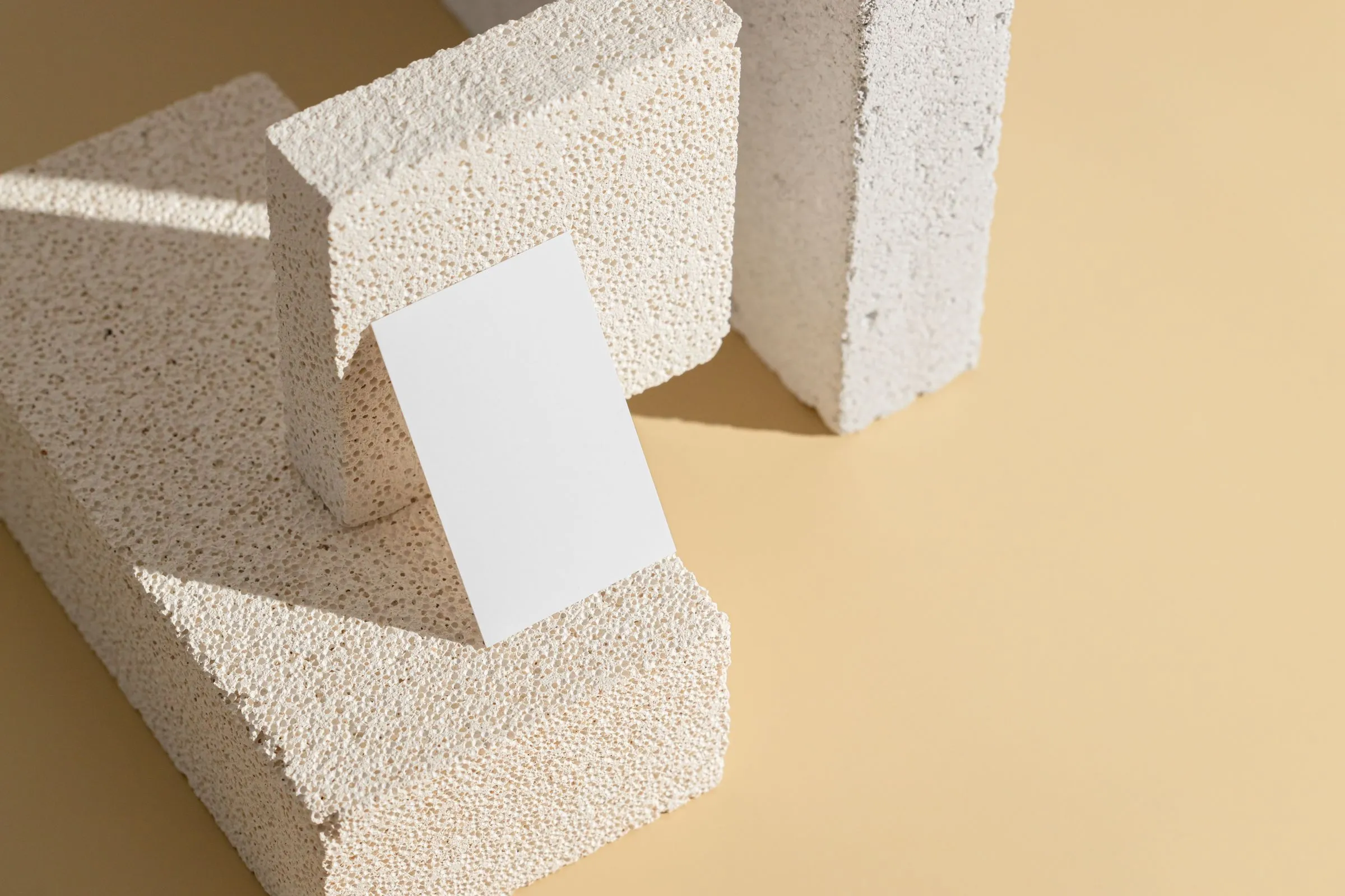 White porous building blocks arranged on a sand-coloured surface with a blank card among them.