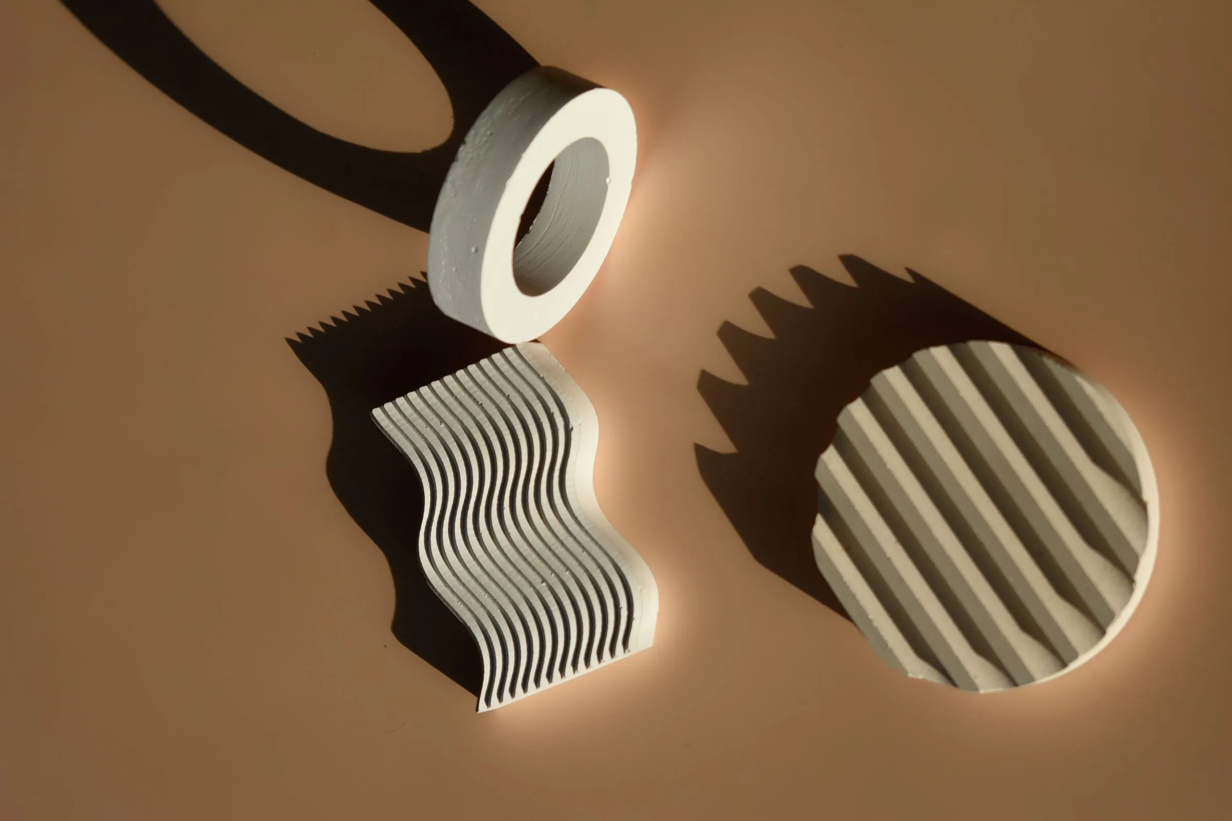 Three white ridged plaster shapes casting long shadows on a warm tan surface.