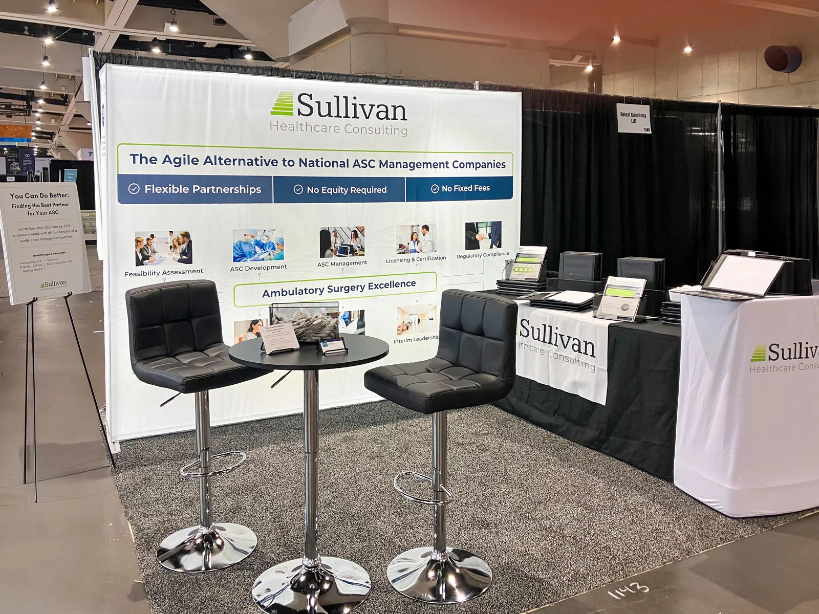 The Sullivan Healthcare Consulting booth installed at a trade show: a backdrop reading "The Agile Alternative to National ASC Management Companies" with bar stools, a table and branded table covers.