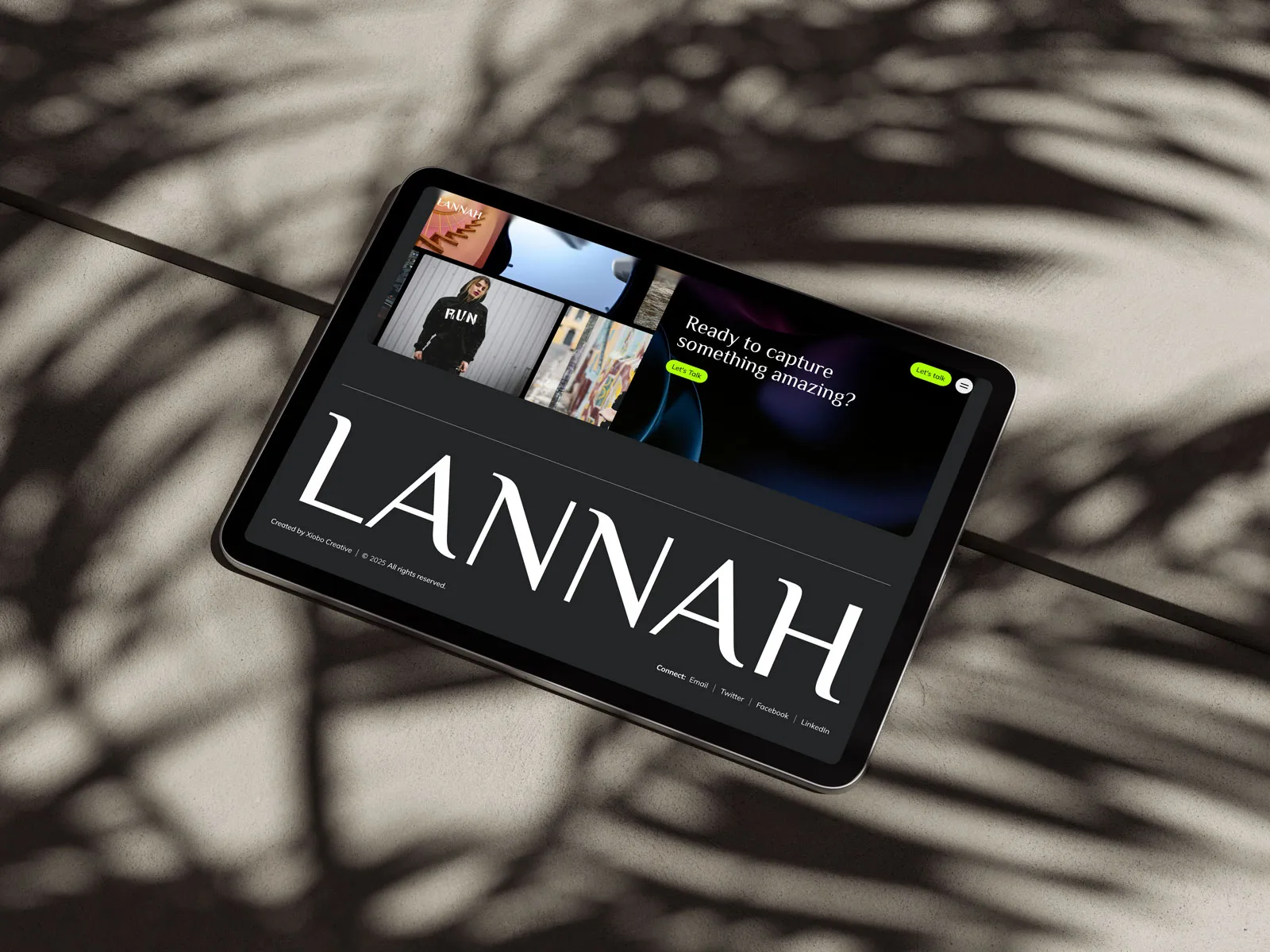 Tablet in palm-leaf shadows showing the Lannah website with a large wordmark and photo grid.