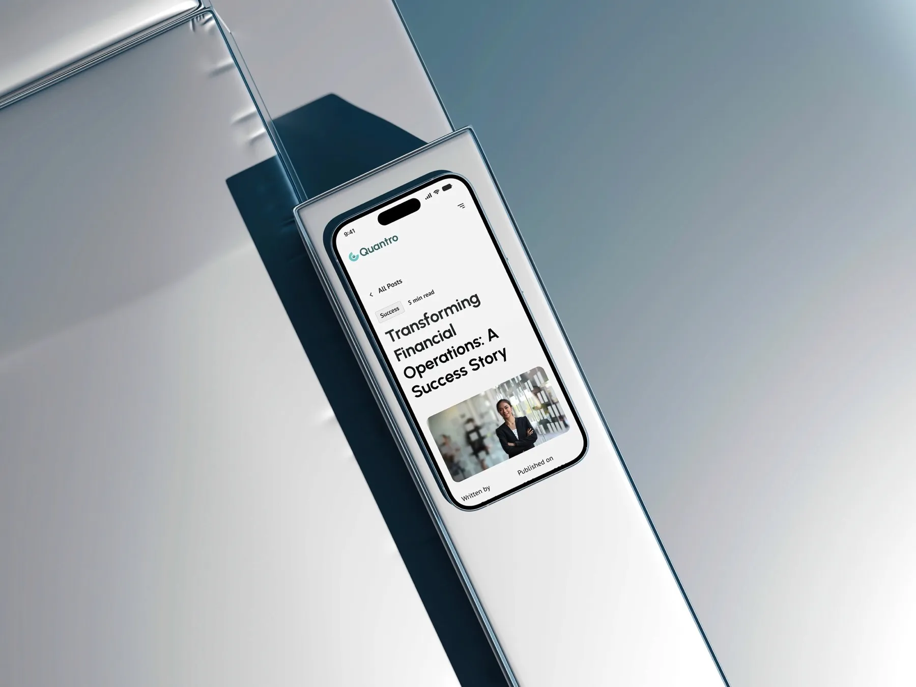 Phone leaning on a glass panel showing a Quantro blog post, "Transforming Financial Operations: A Success Story".