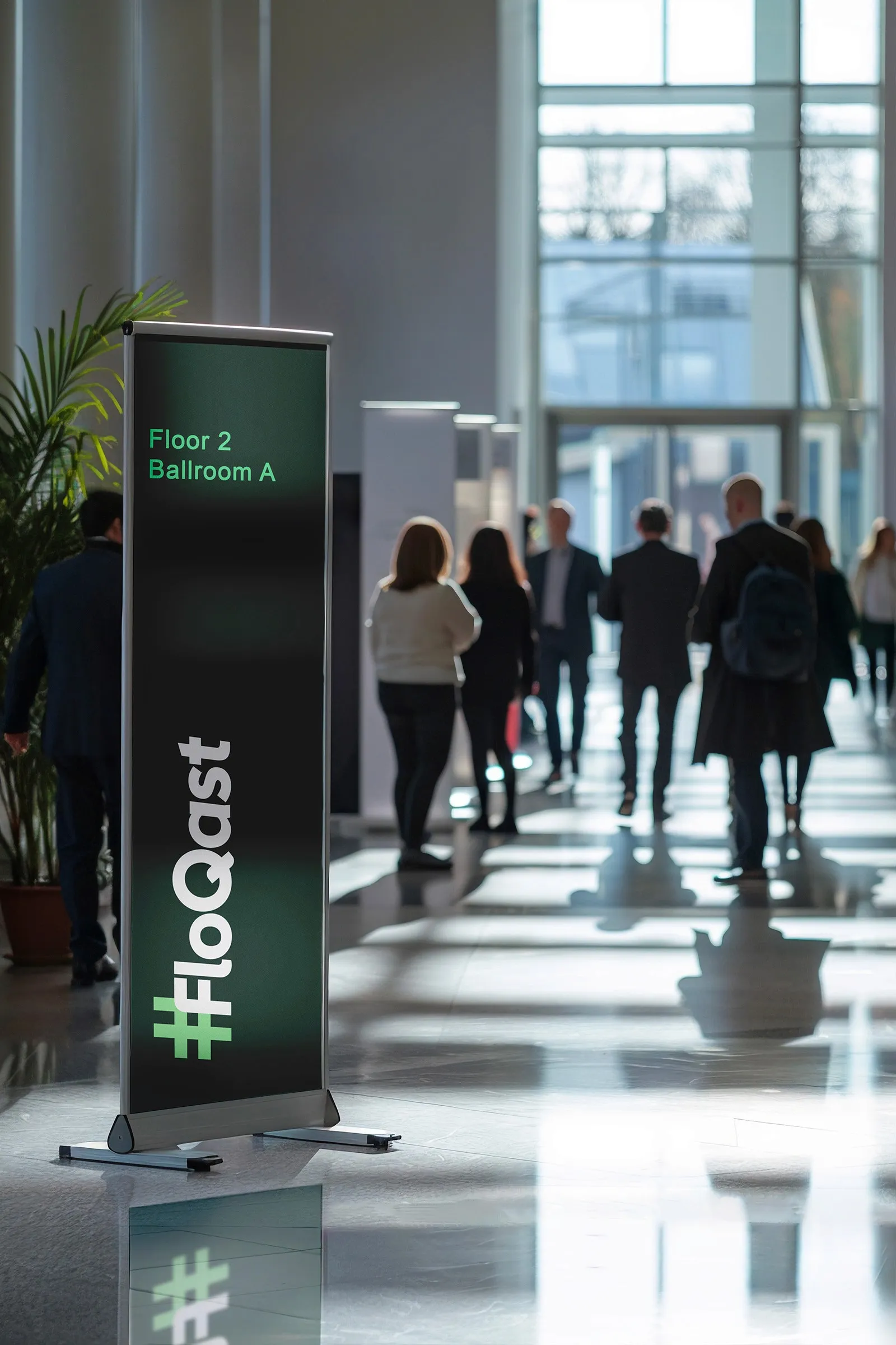 FloQast pull-up banner in a conference hallway pointing attendees to Floor 2, Ballroom A.