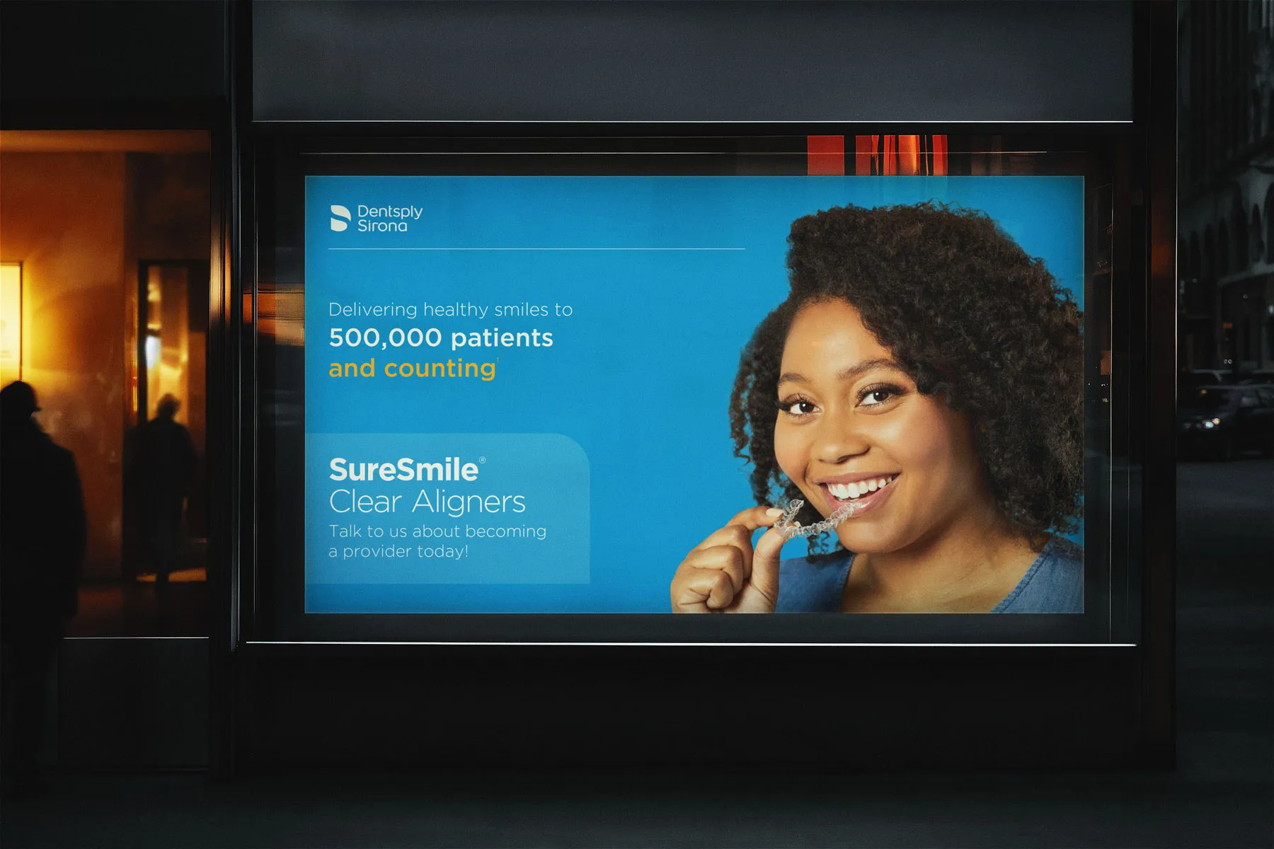 Night-time shelter ad of a woman holding a clear aligner: "Delivering healthy smiles to 500,000 patients and counting".