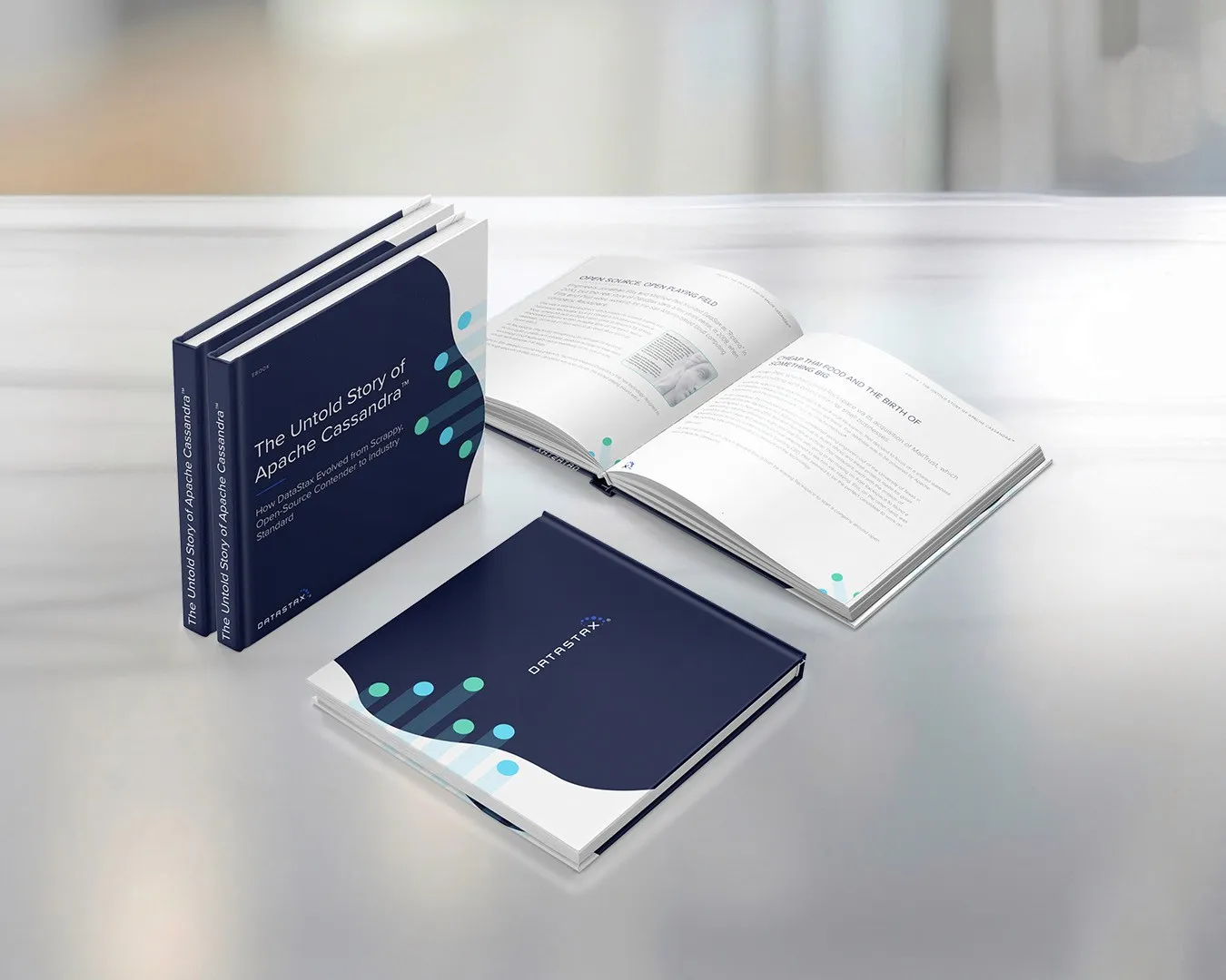 Printed copies of the DataStax eBook “The Untold Story of Apache Cassandra” in navy with teal dots, one open to an inside spread.