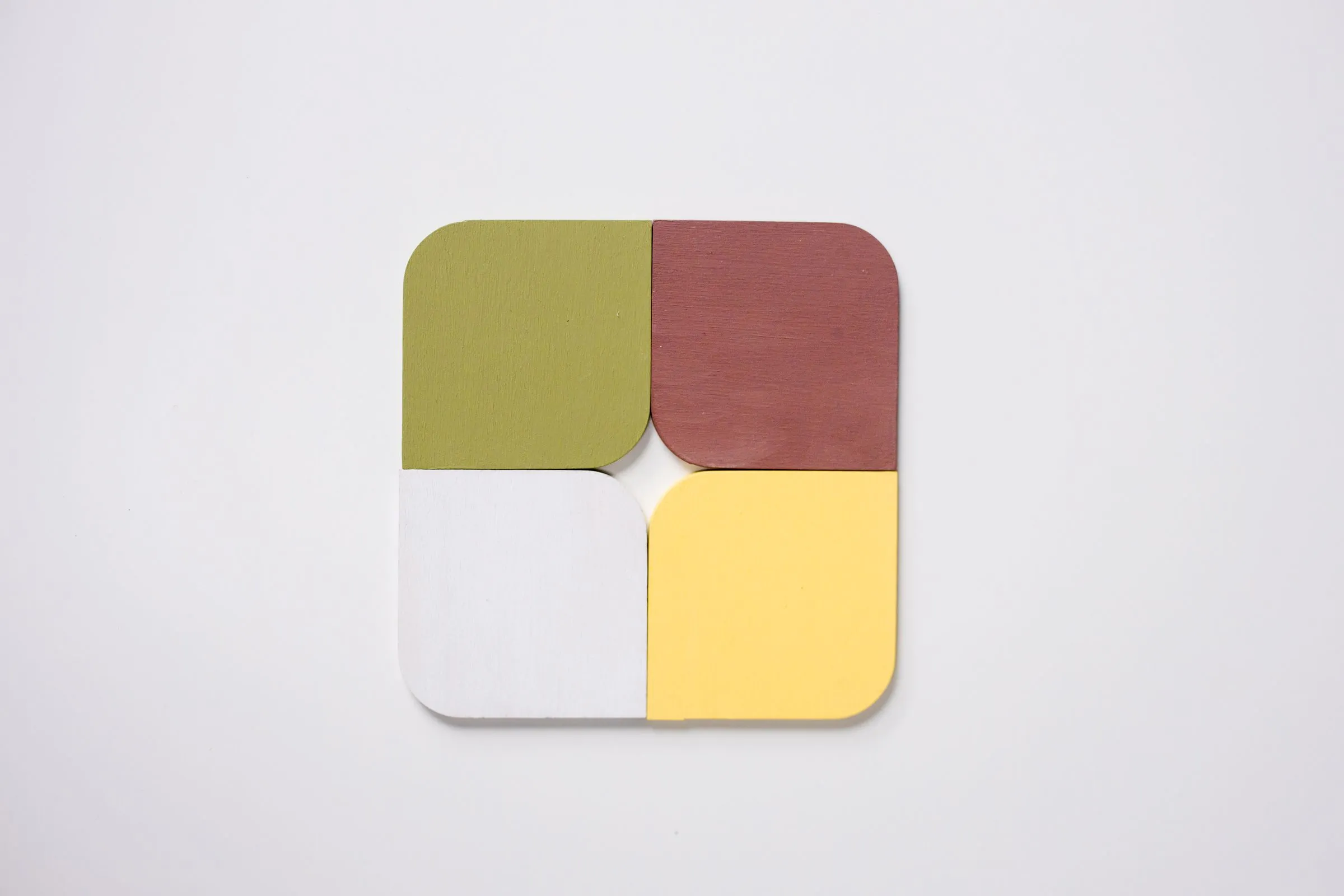 Four rounded colour tiles in olive, brick red, white and pale yellow joined into a square on white.