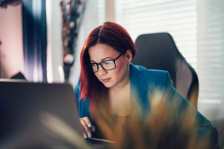 Ingrid Altreche, with red hair and glasses, working at a laptop in a softly lit office.