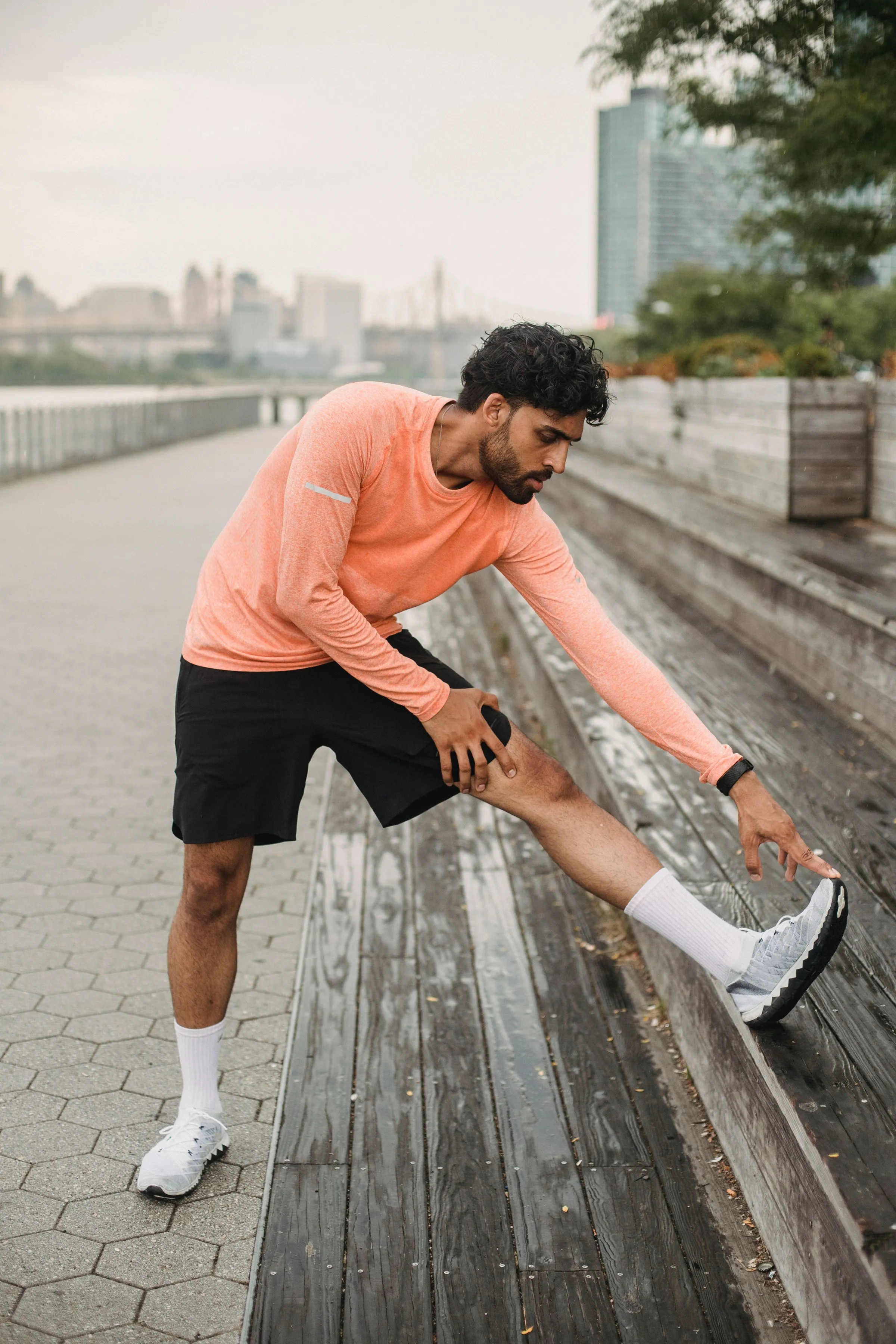 A runner stretching his hamstring on a bench by the river.