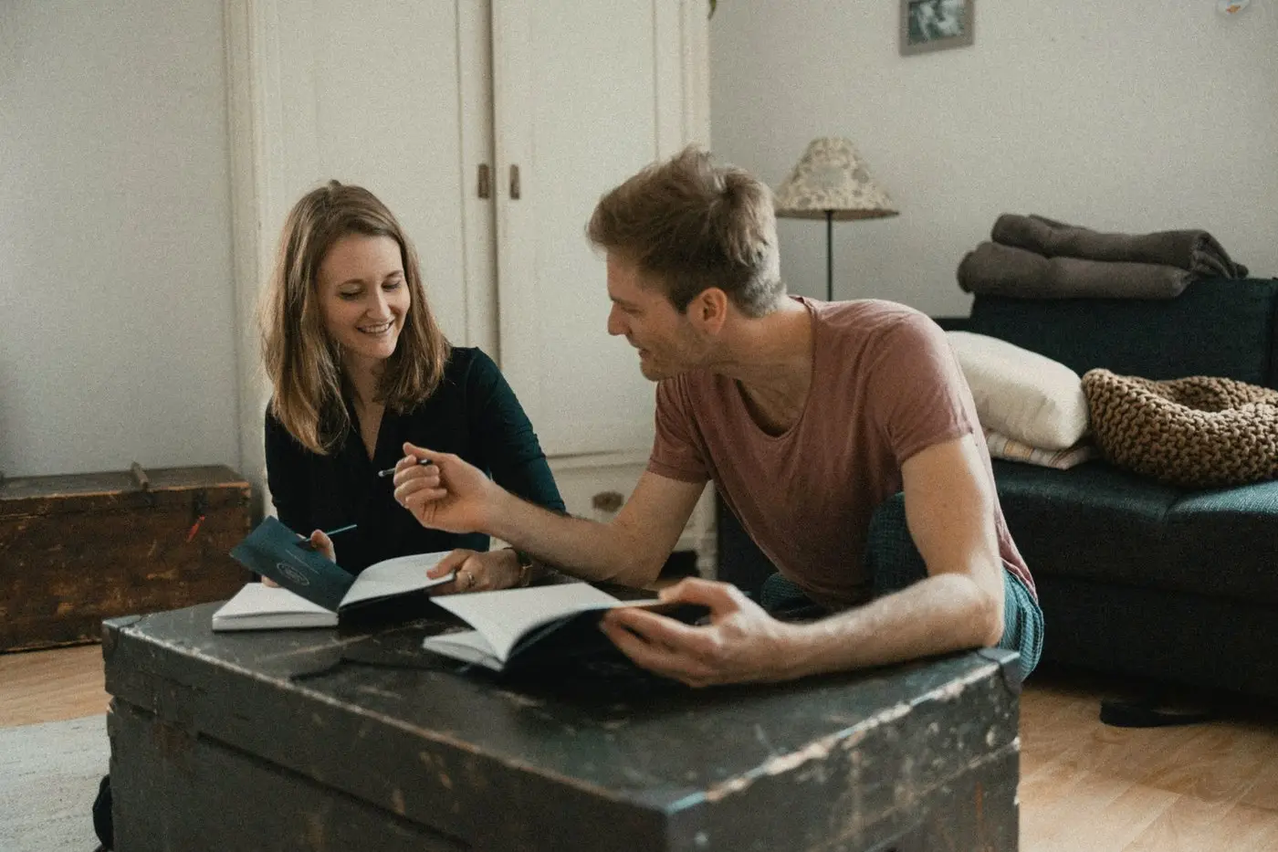 A couple going over notebooks together at a wooden trunk in their living room, laughing