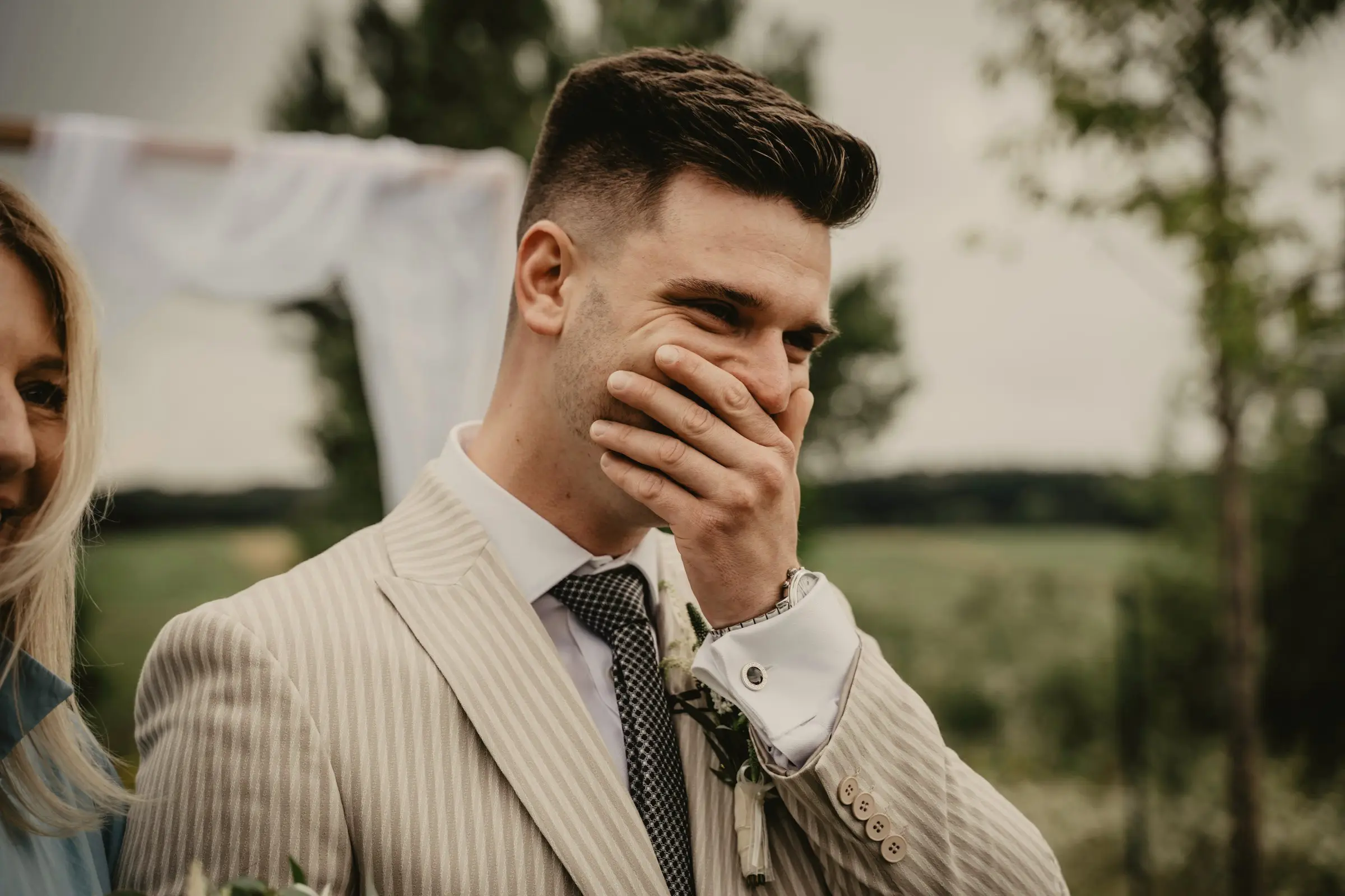 Groom covers his mouth with his hand, visibly moved, during the outdoor ceremony.