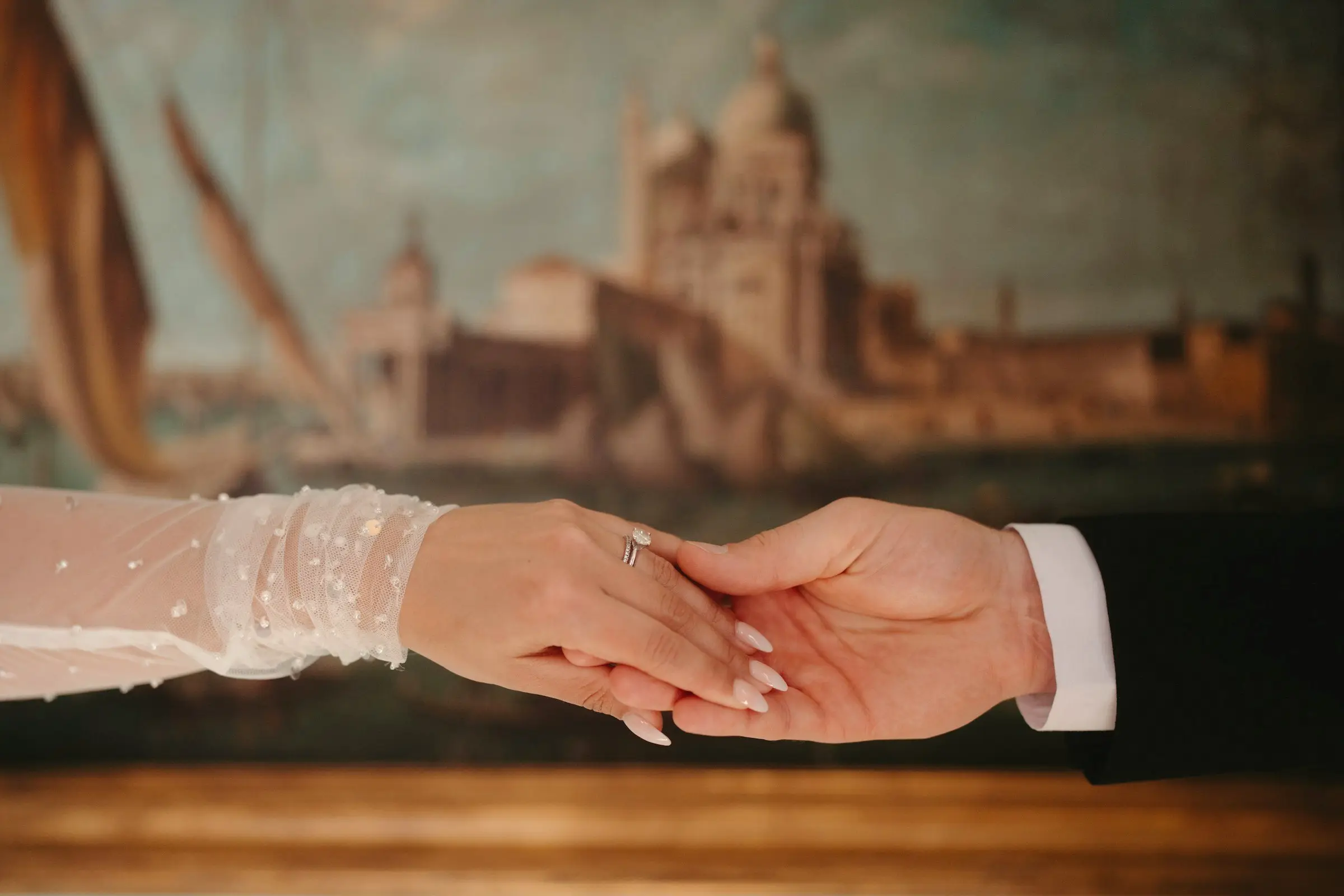 Bride and groom’s clasped hands in front of a classical painting of Venice, warm museum light
