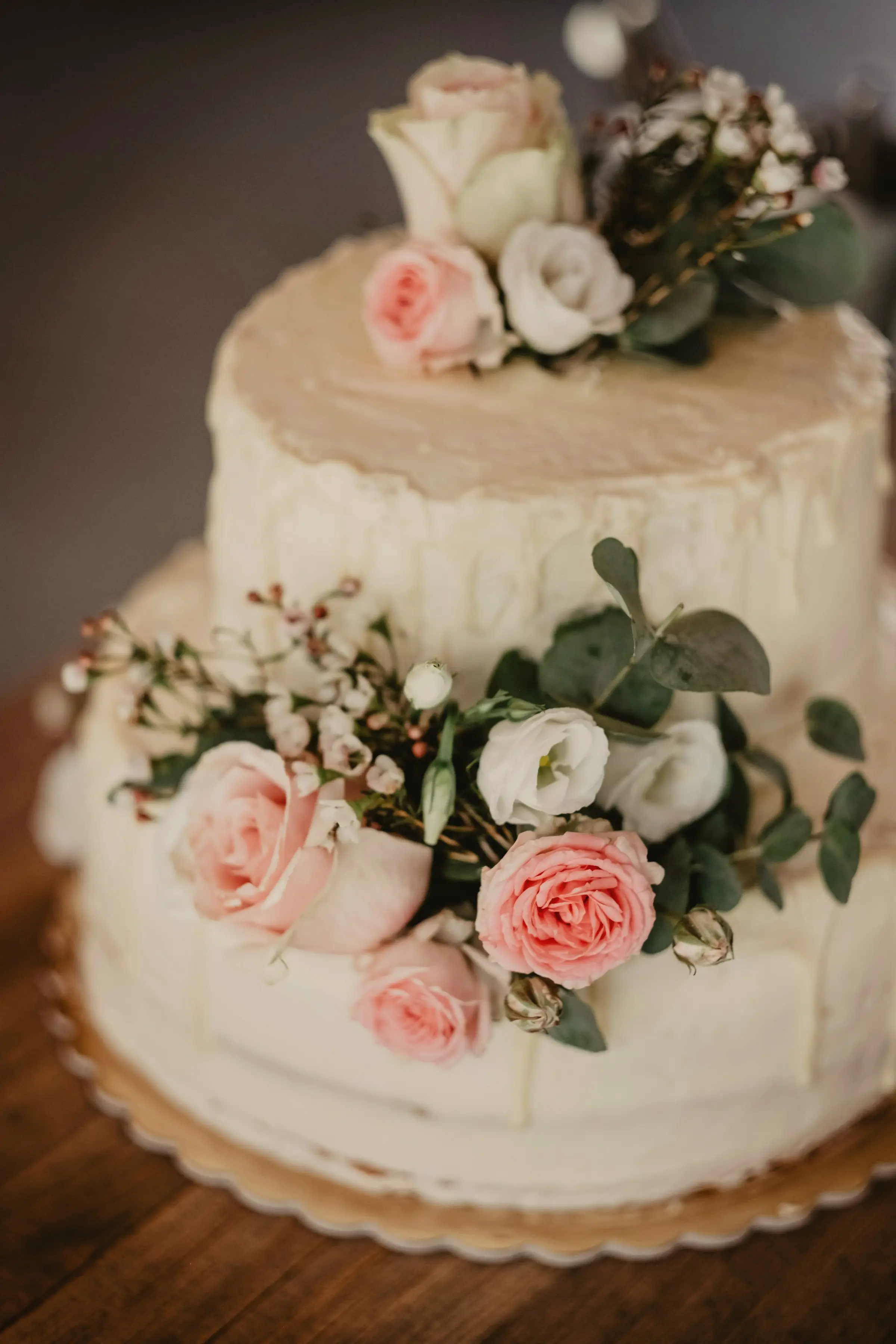 Simple white wedding cake decorated with pink and cream roses and greenery on a wooden table