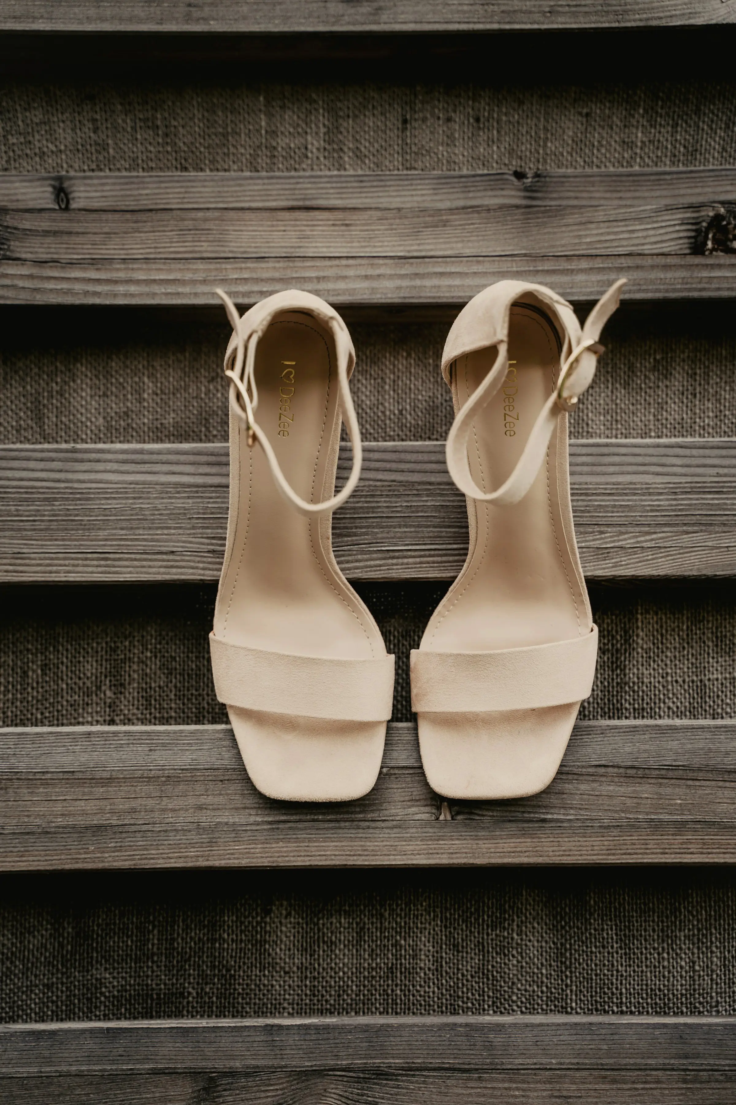 Nude block-heel bridal sandals hanging against weathered grey wooden slats