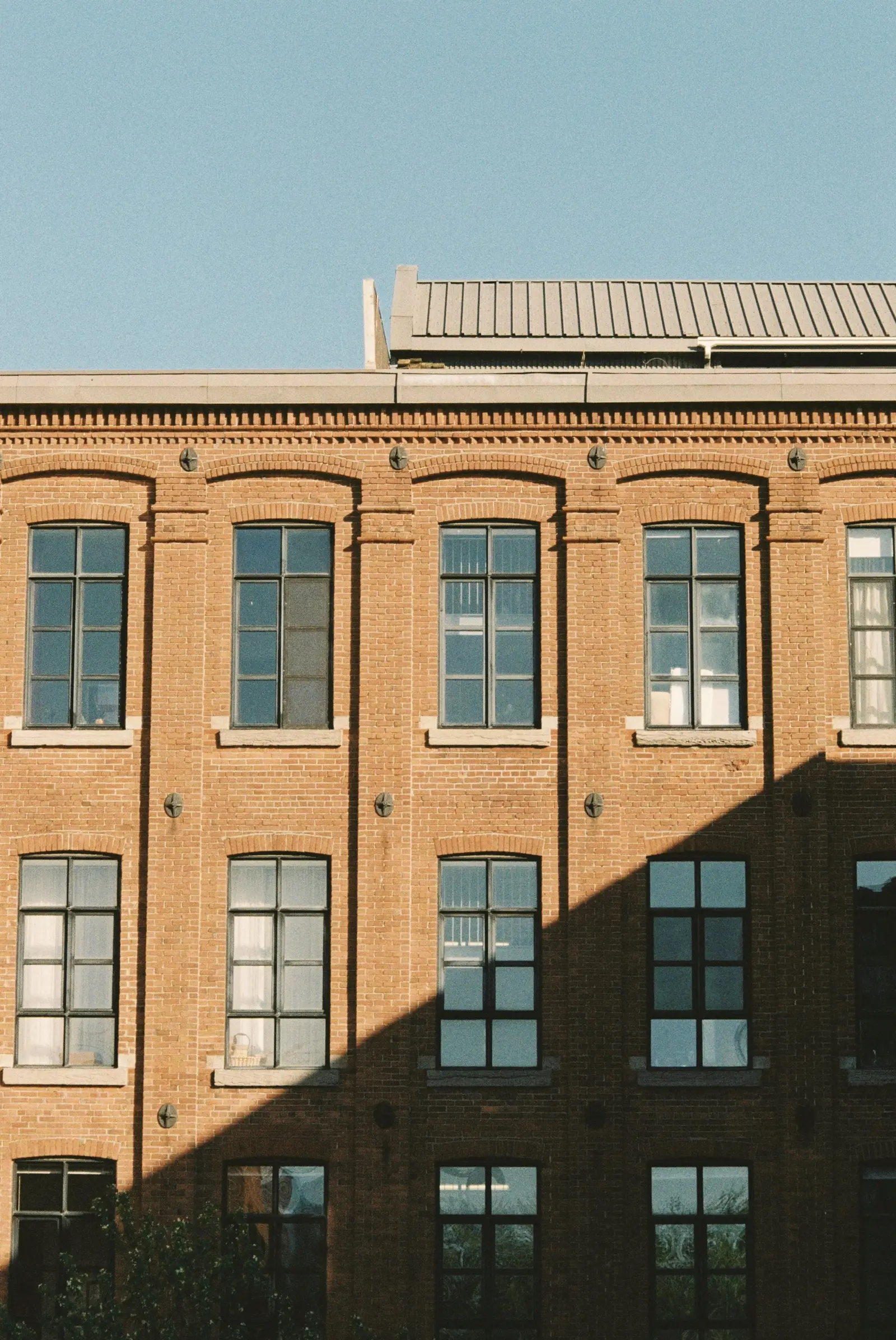 Restored red-brick building with rows of tall windows against a blue sky.