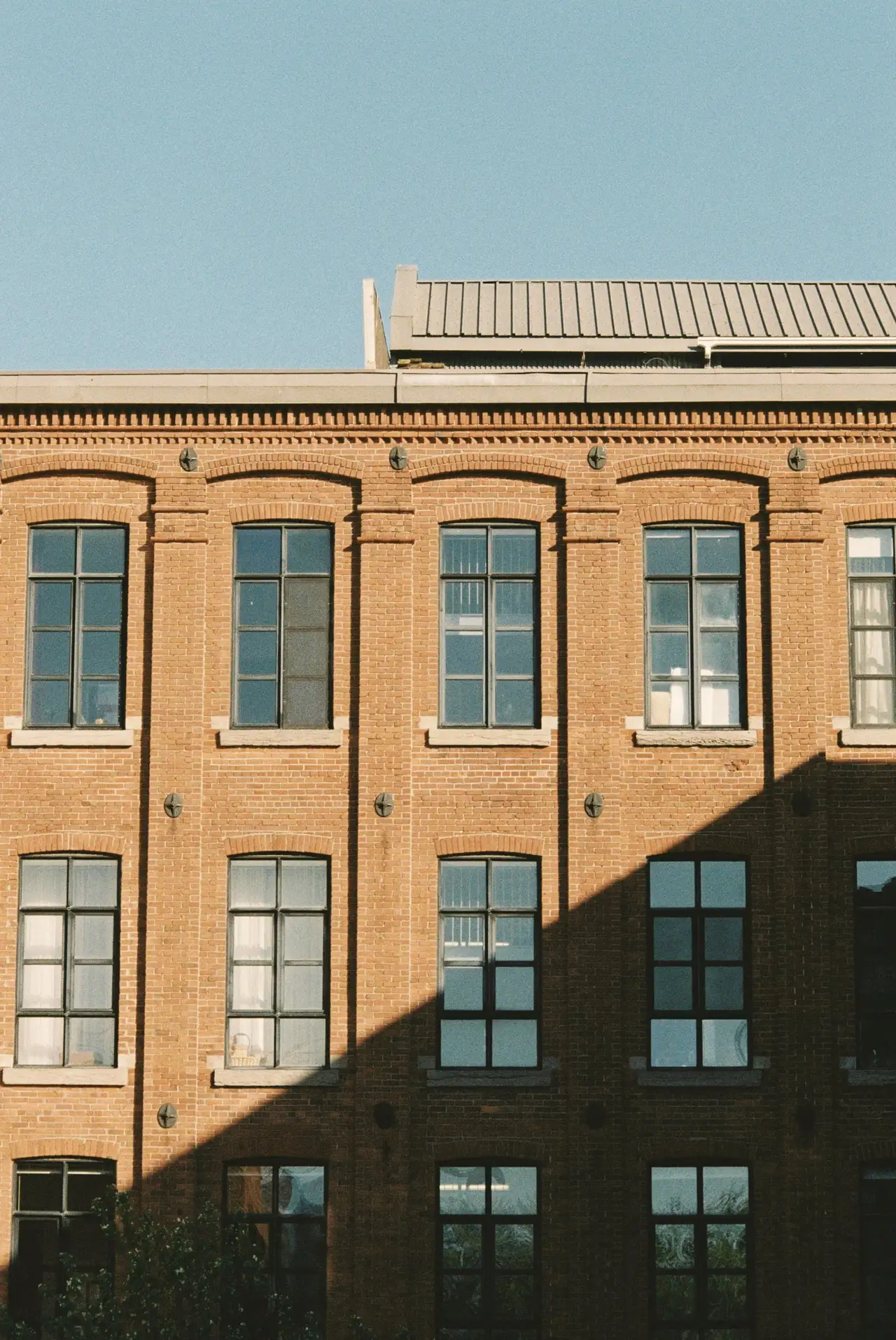 Restored red-brick building with rows of tall windows against a blue sky.
