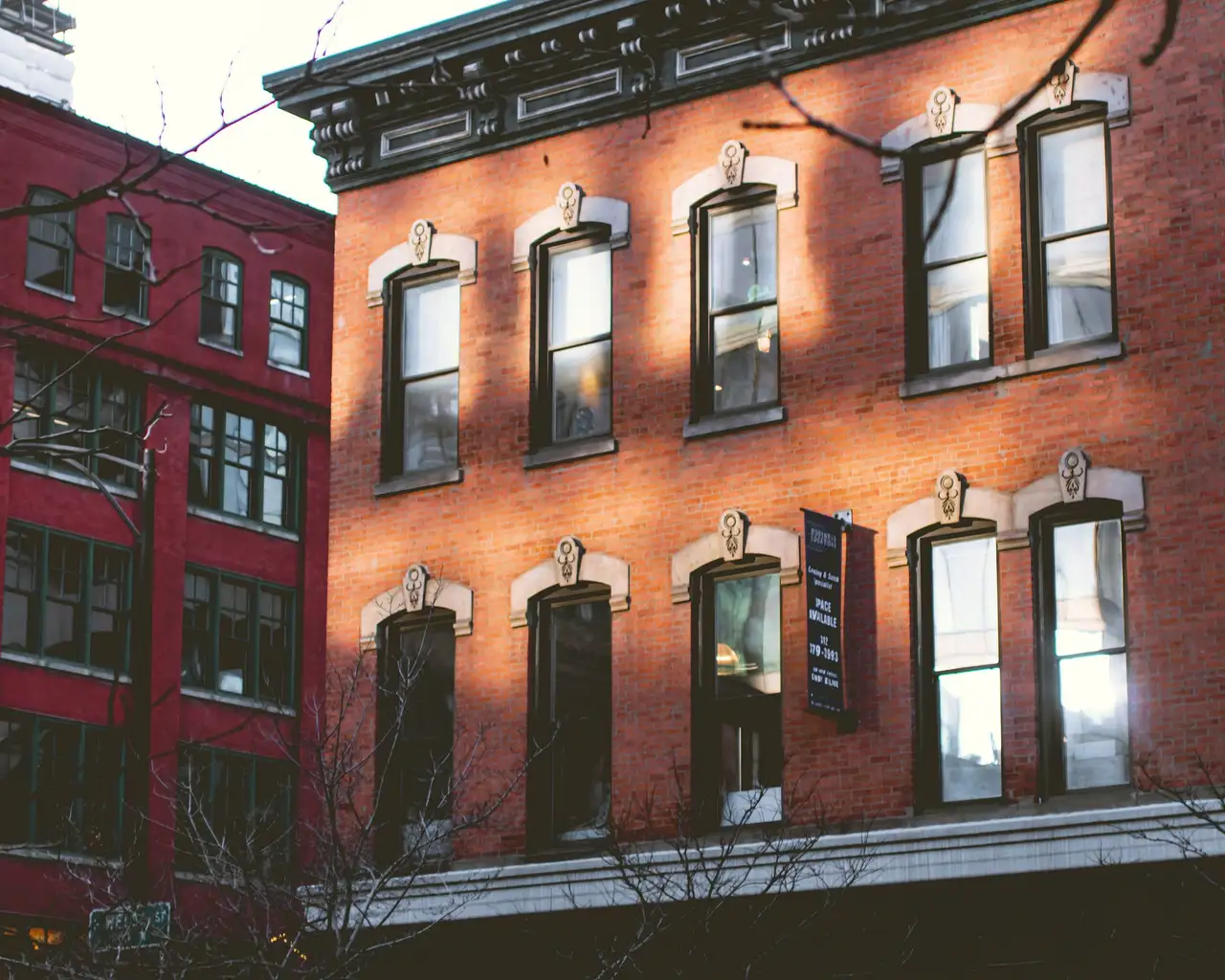 Three-story red-brick building with tall windows under carved stone hoods, afternoon sun across the front.