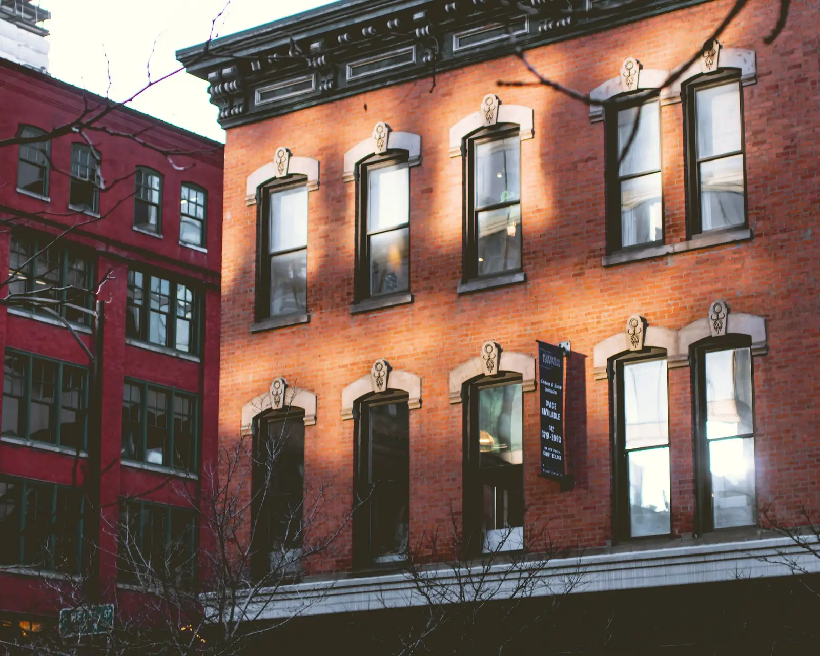 Three-story red-brick building with tall windows under carved stone hoods, afternoon sun across the front.