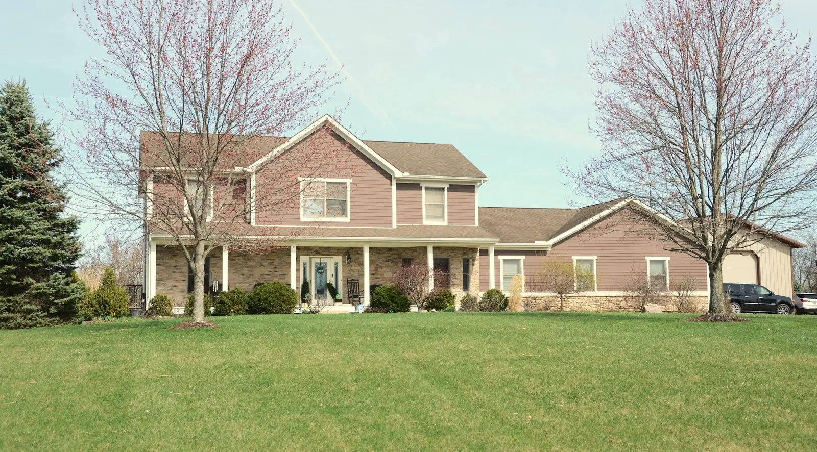 Two-story house with brick and tan siding, a covered front porch and an attached garage behind a wide lawn.