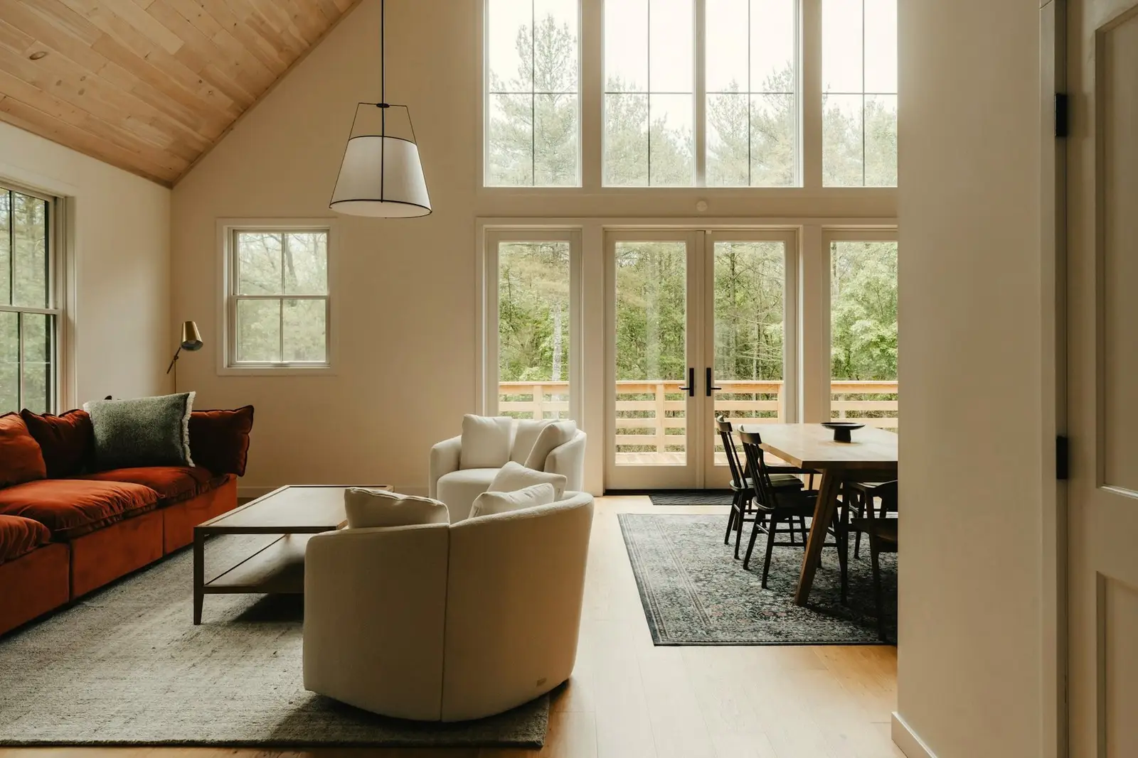 Vaulted living room with a white-oak ceiling, a rust sofa and tall windows, photographed for a listing.