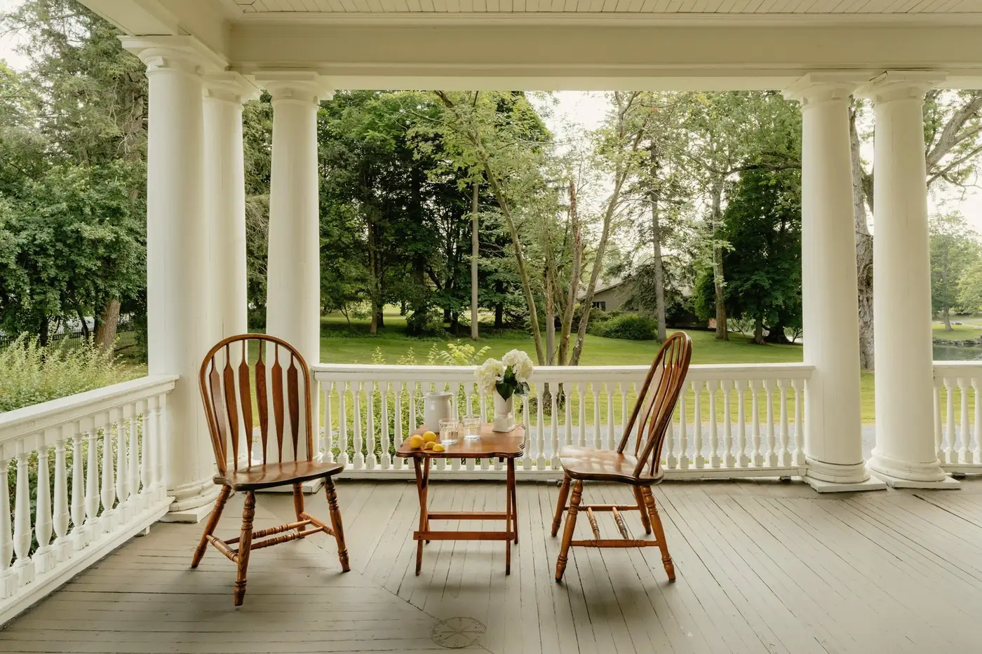 A covered front porch with white columns and wooden chairs looking out over a green lawn.