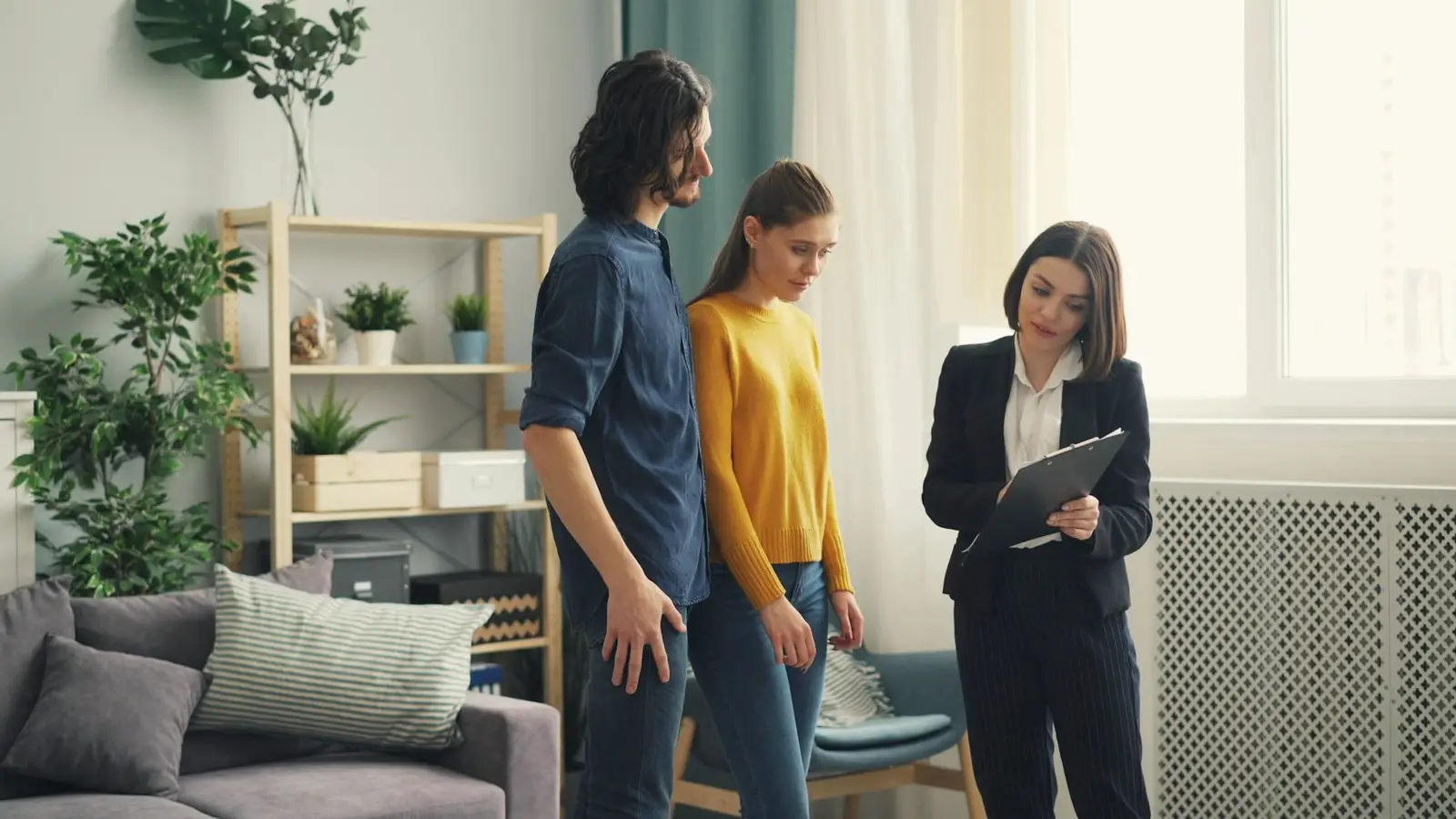 A Realtor with a clipboard showing a bright living room to a young couple.