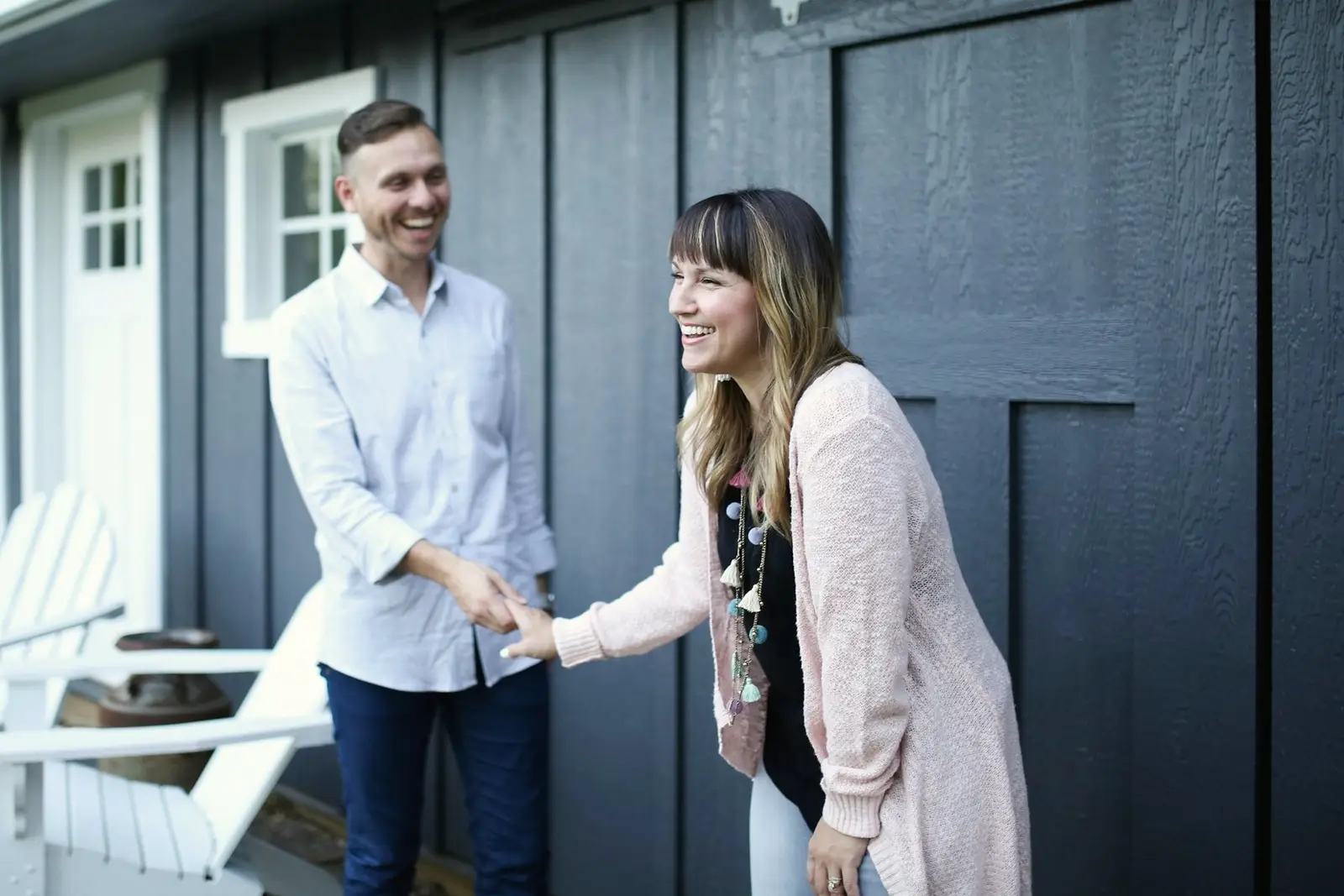 A Realtor shaking hands with a smiling client outside the front door of a dark-sided house.
