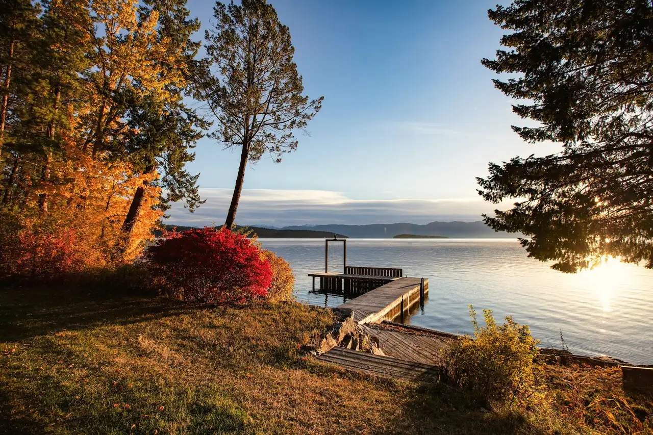 A small wooden dock on a calm lake at golden hour, red and orange autumn trees on the shore.