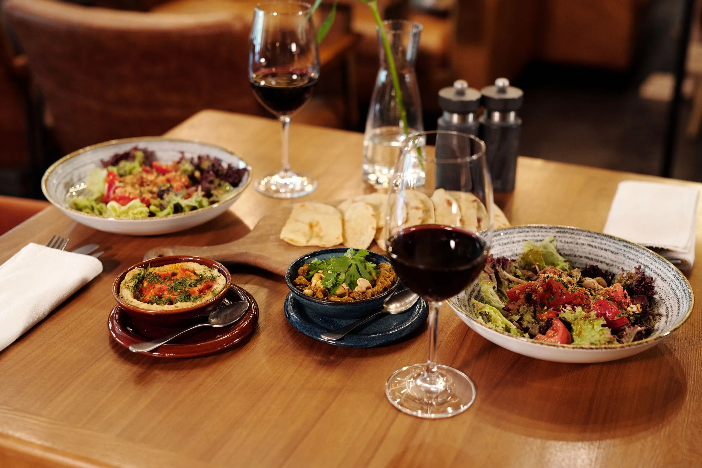 Salads, hummus and flatbread with red wine on a wooden table.