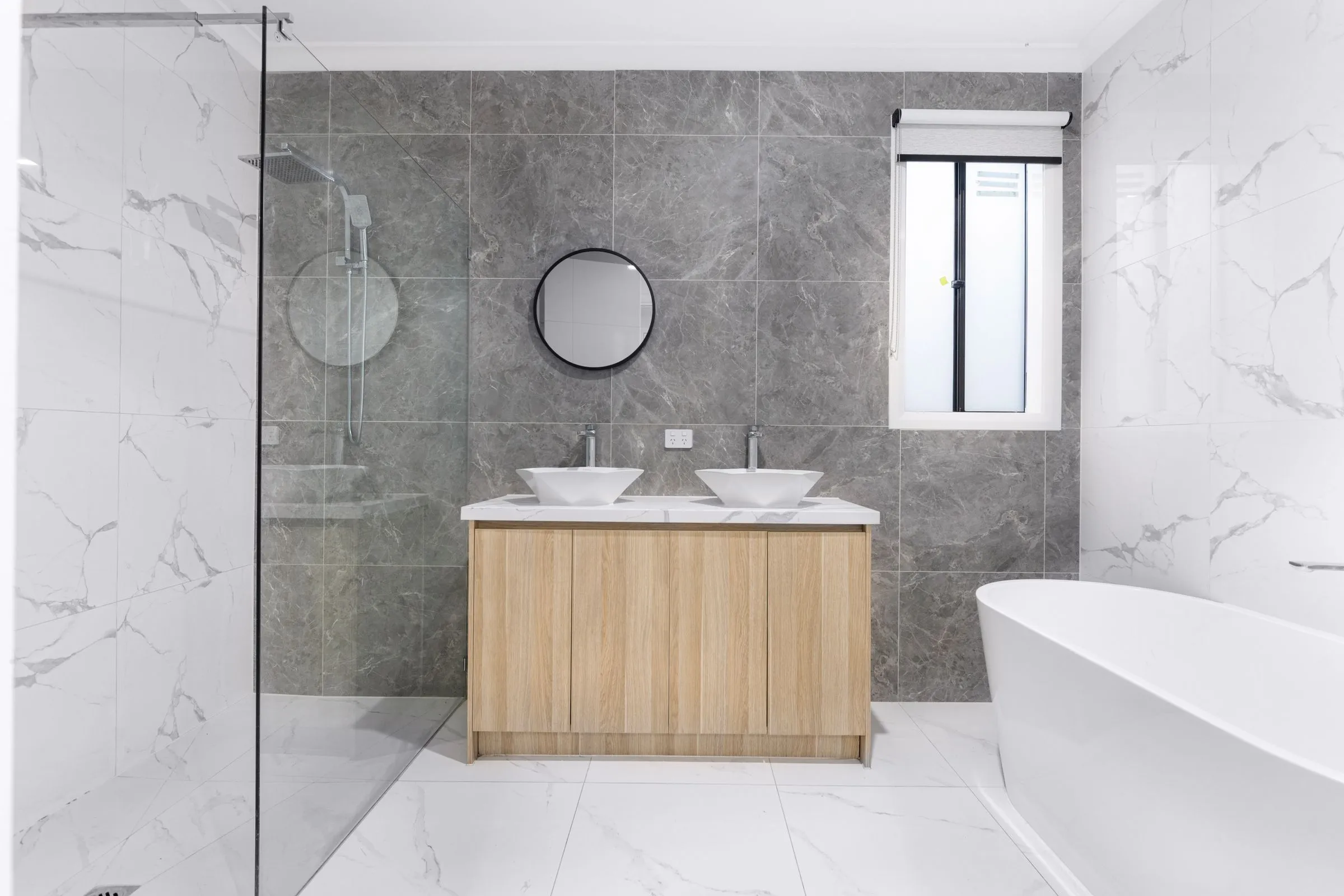 A bright marble bathroom with a freestanding tub and a wood vanity.