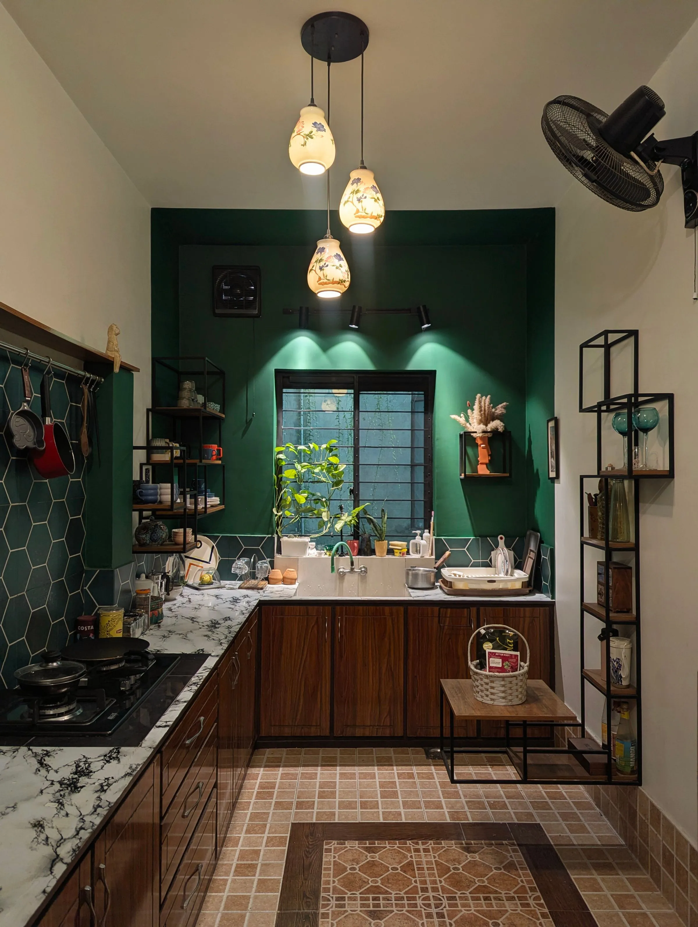 A kitchen with a deep green wall, wood cabinets and patterned floor tile.