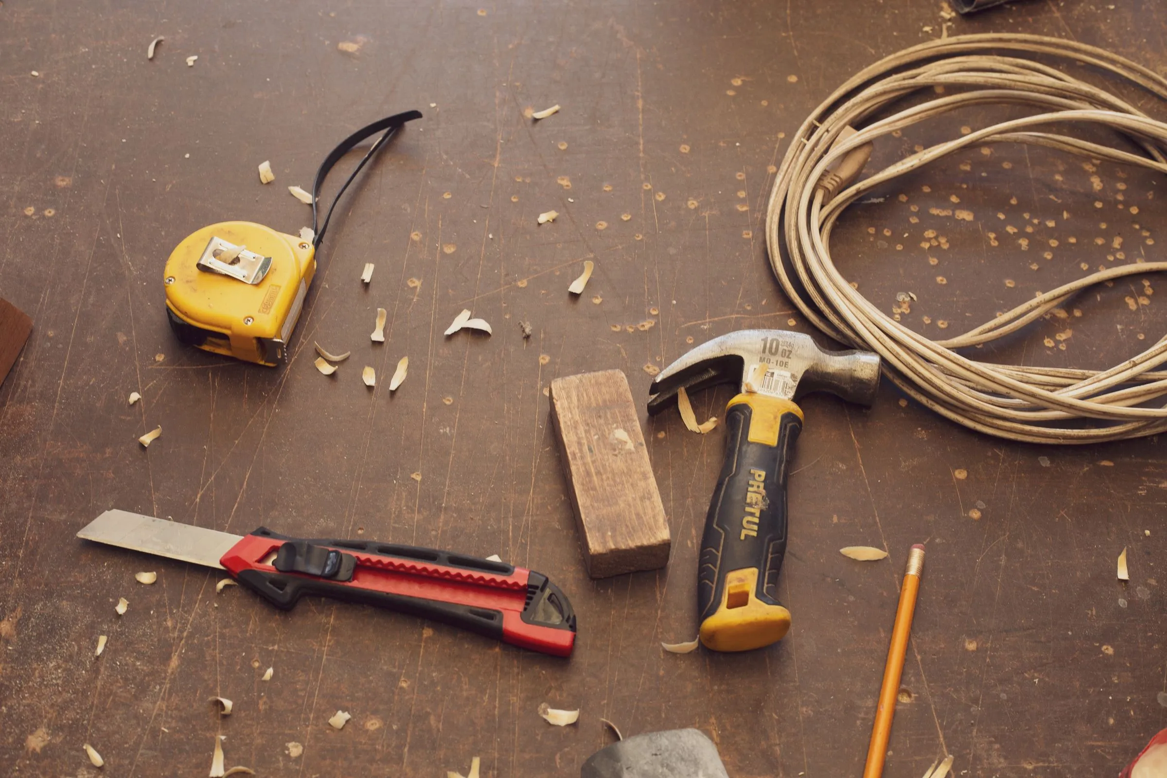 A tape measure, hammer and utility knife on a dusty floor.