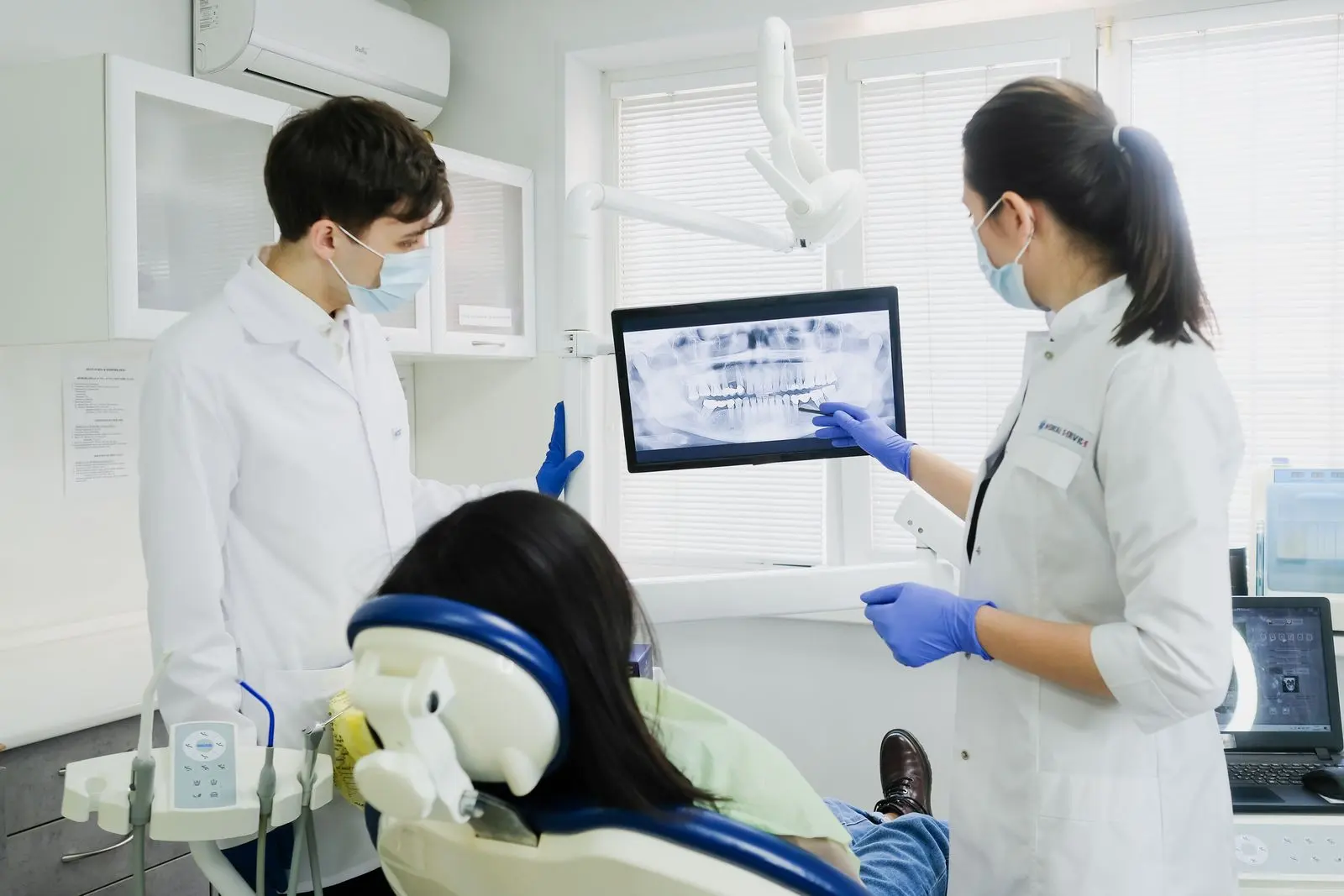 A dentist showing a patient an X-ray on a screen beside the dental chair