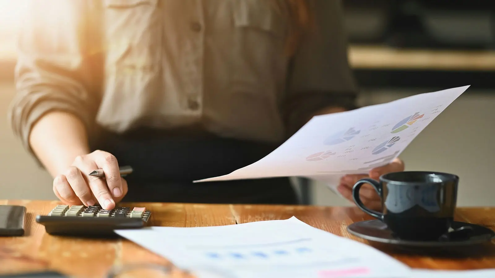 Hands working through tax documents with a calculator and a cup of coffee